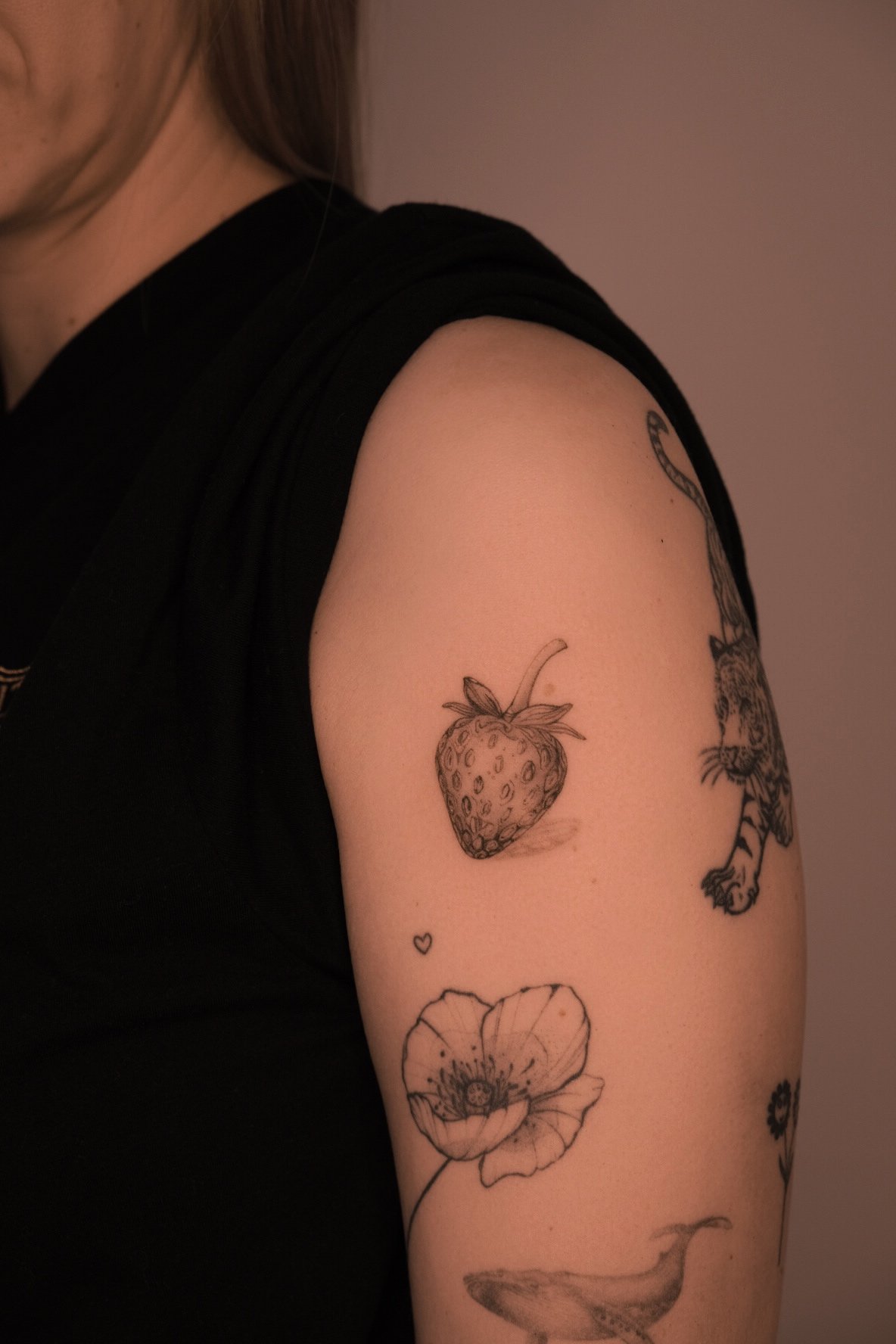 Erdbeere – Mikro-Realismus Fineline-Tattoo am Oberarm; zarte Schattierung, präzise Details – Tattoo Artist in Wien.