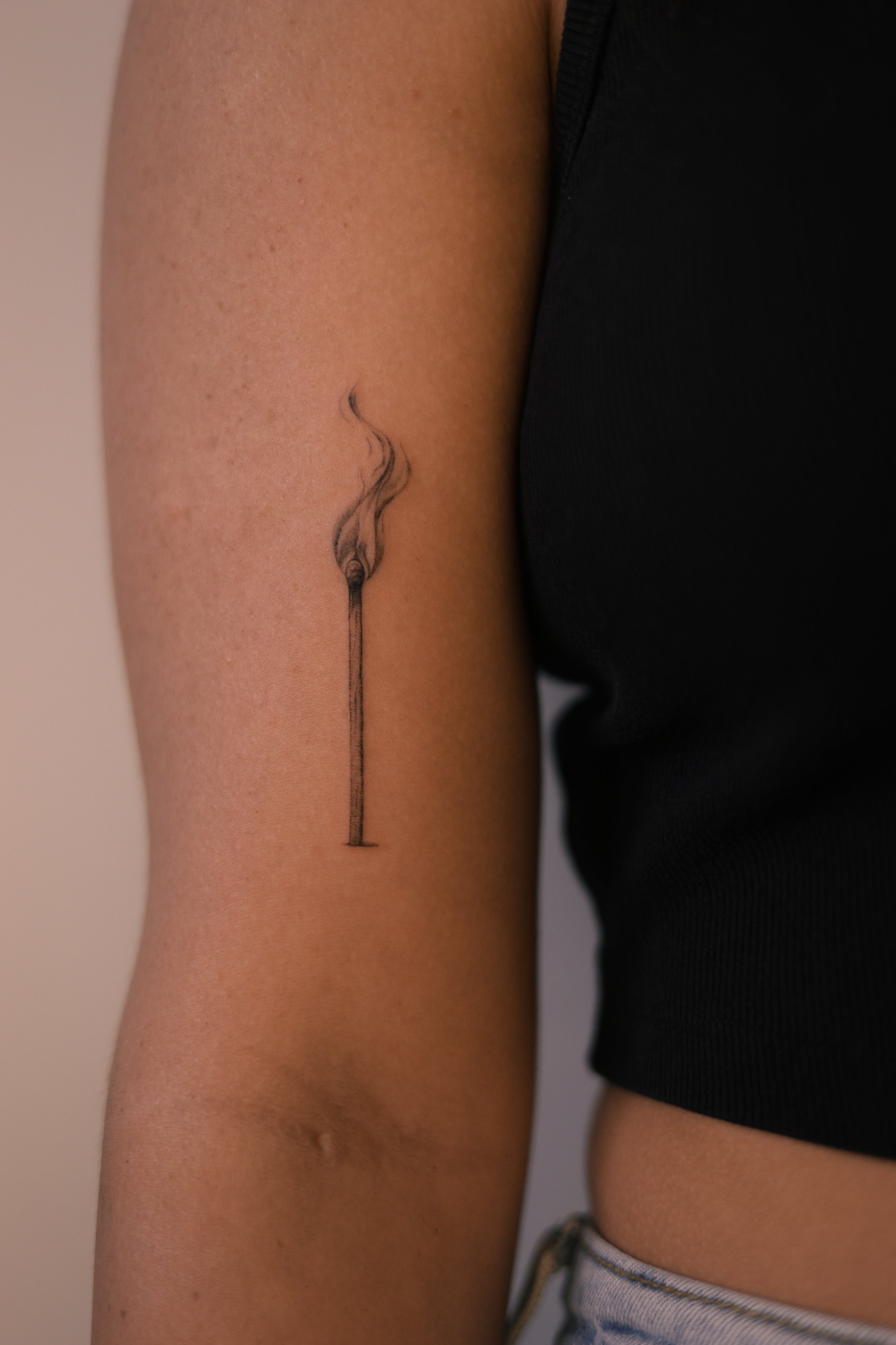 Delicate fine line micro realism matchstick tattoo with soft flame detail on inner arm, created by tattoo artist in Vienna