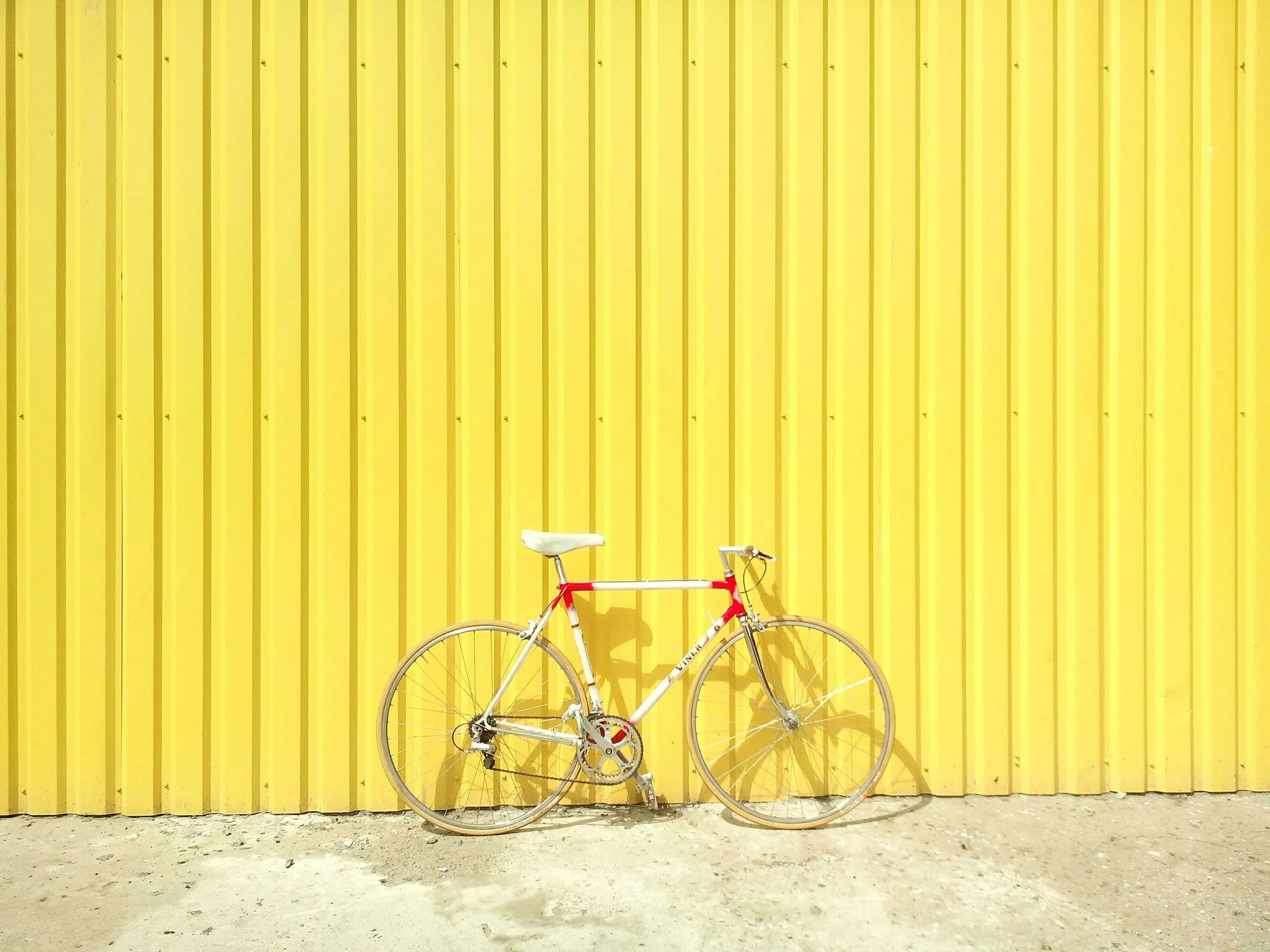 A white and red bicycle leaning against a yellow, corrugated metal wall.