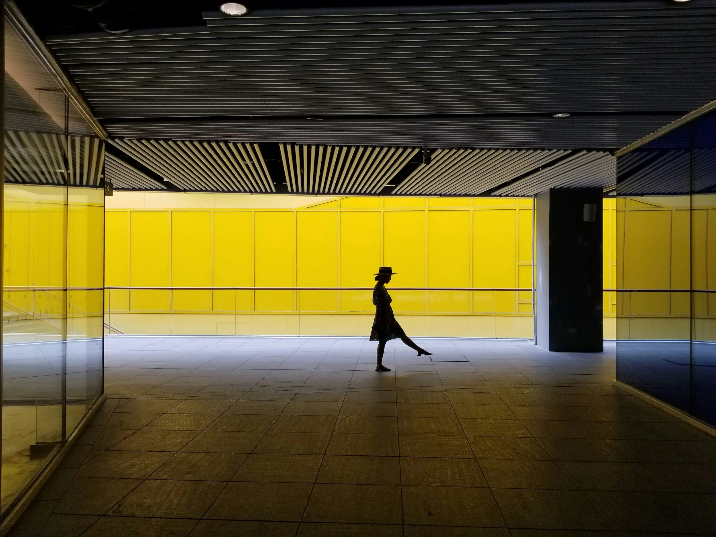 A person walking in an indoor space with a black ceiling and bright yellow wall in background.