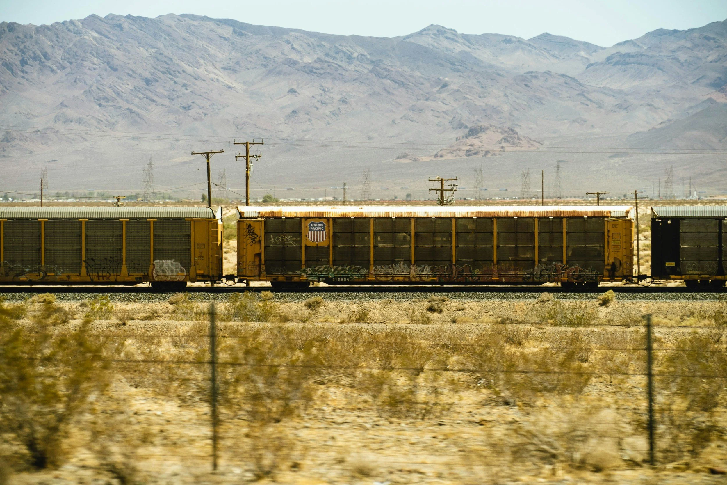 A yellow Union Pacific freight train moving through a desert landscape with distant mountains under a clear sky.
