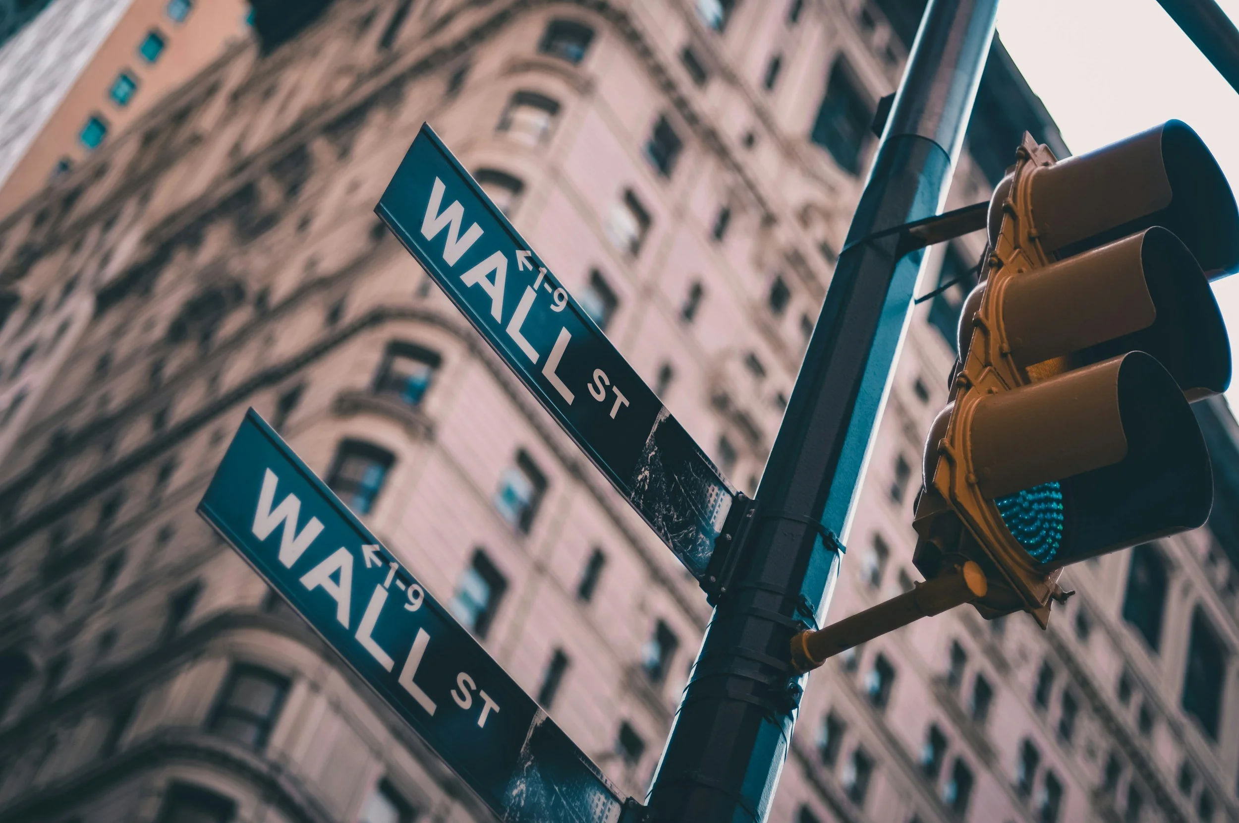Street sign showing 'W 49th St' at an intersection with yellow traffic lights against background of tall city buildings.