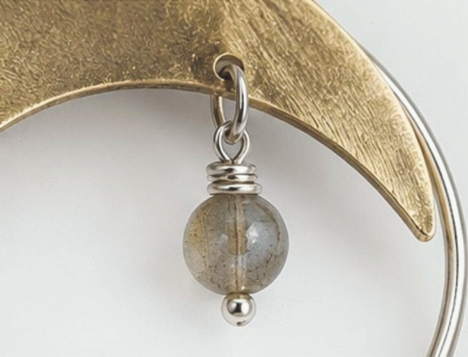 Close-up of labradorite gemstone suspended from brass crescent moon earring