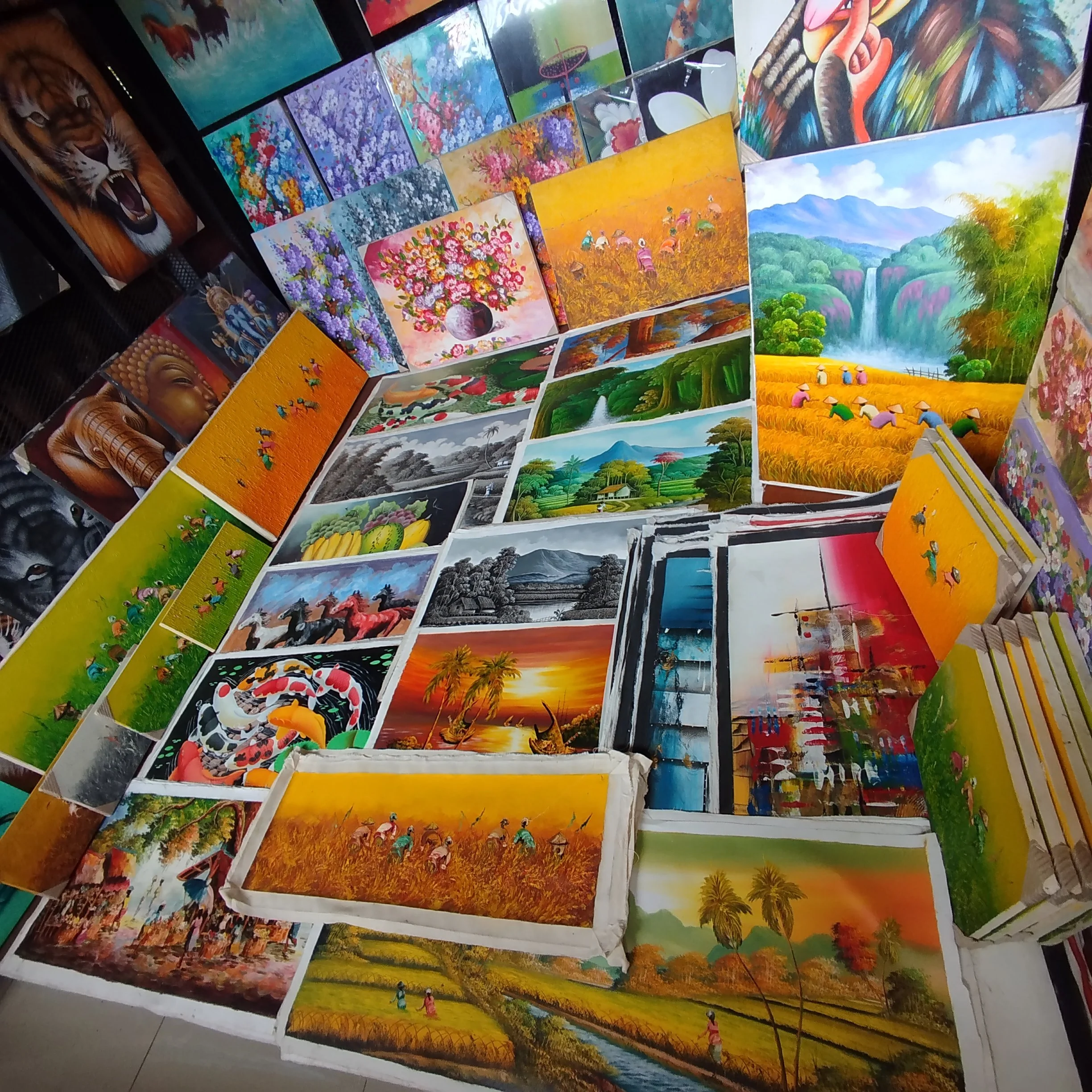 Az Ubudi művészeti piac (Art Market) színes festmények kiállítása, melyek között tájképek, állatok, virágok és kulturális jelenetek is szerepelnek, asztalokon és falakon elrendezve.