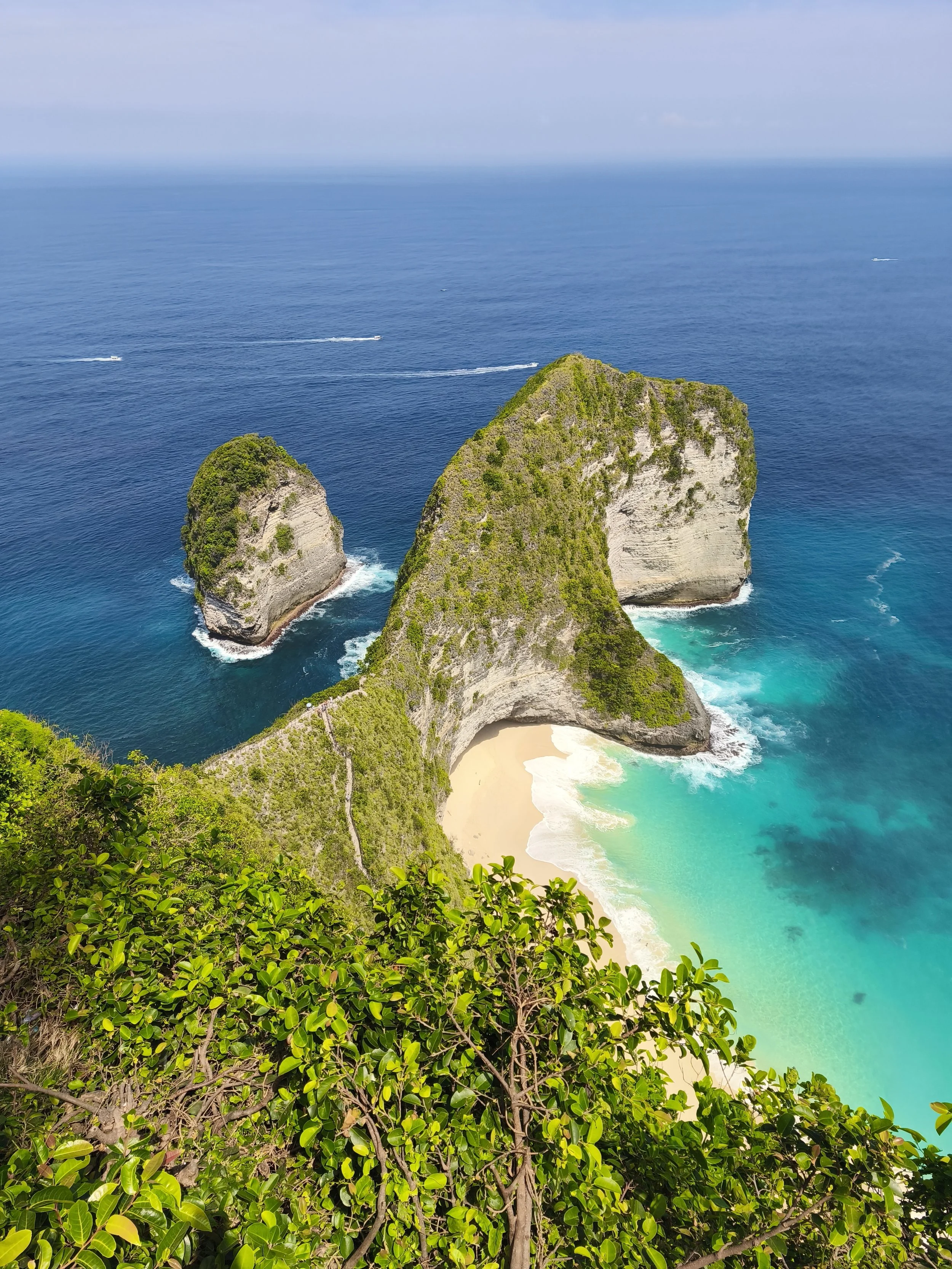 Aerial view of a tropical beach with turquoise waters surrounded by lush green cliffs and rock formations.