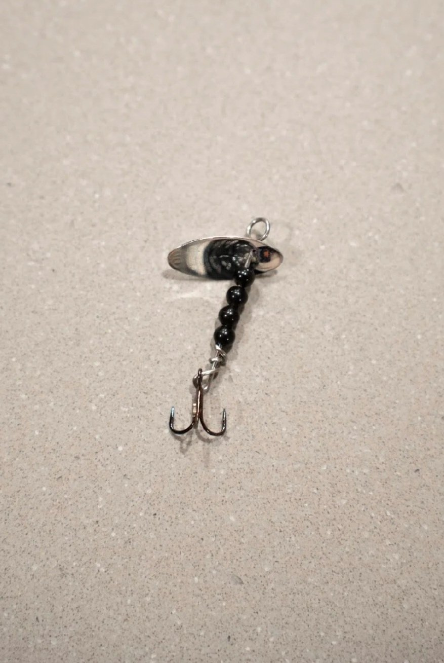 A fishing lure with a black and white fish head, black beads, and two small hooks on a light gray surface.