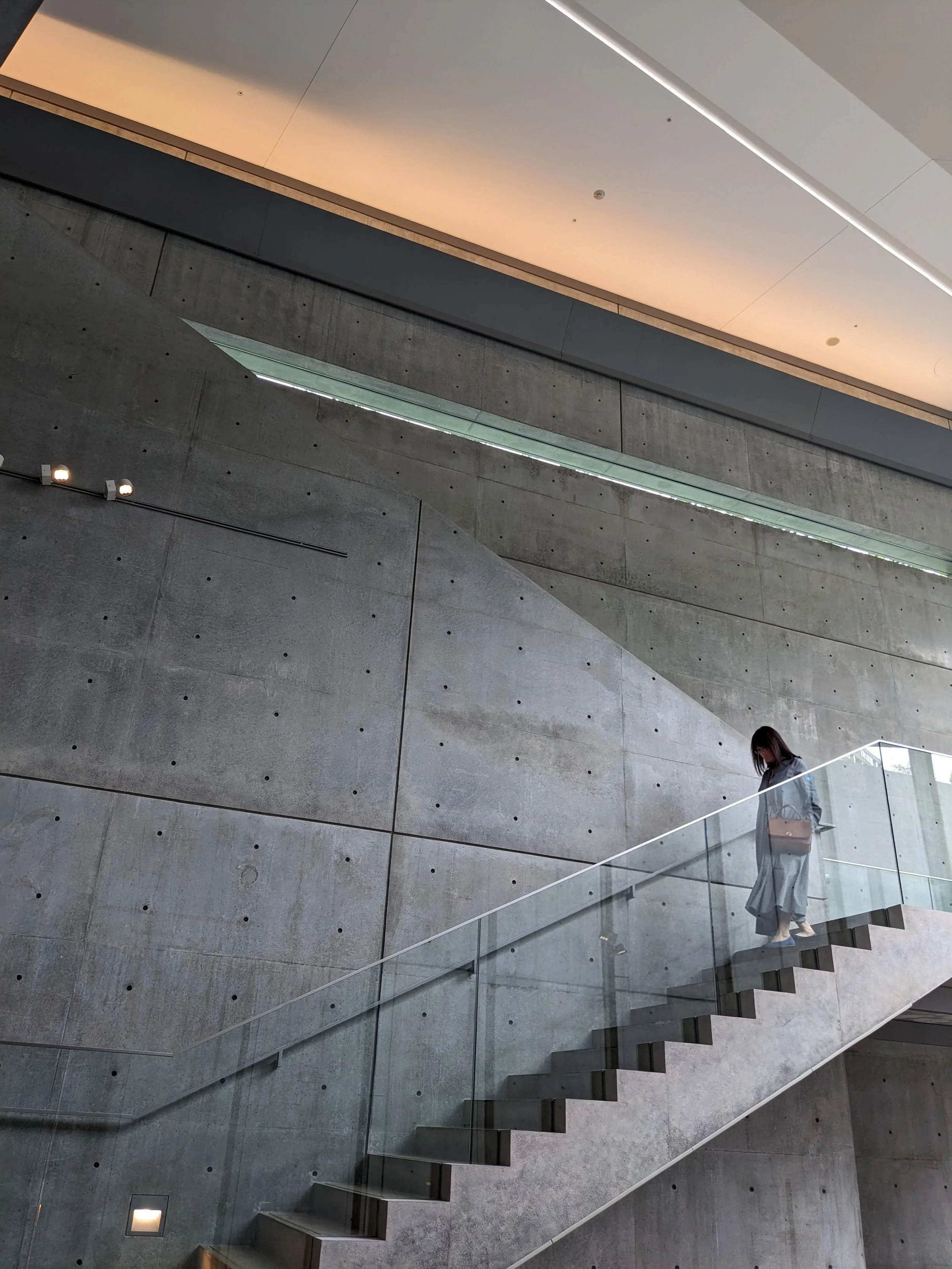 A person walking down a modern concrete staircase with glass railings in a contemporary building with minimalist design.