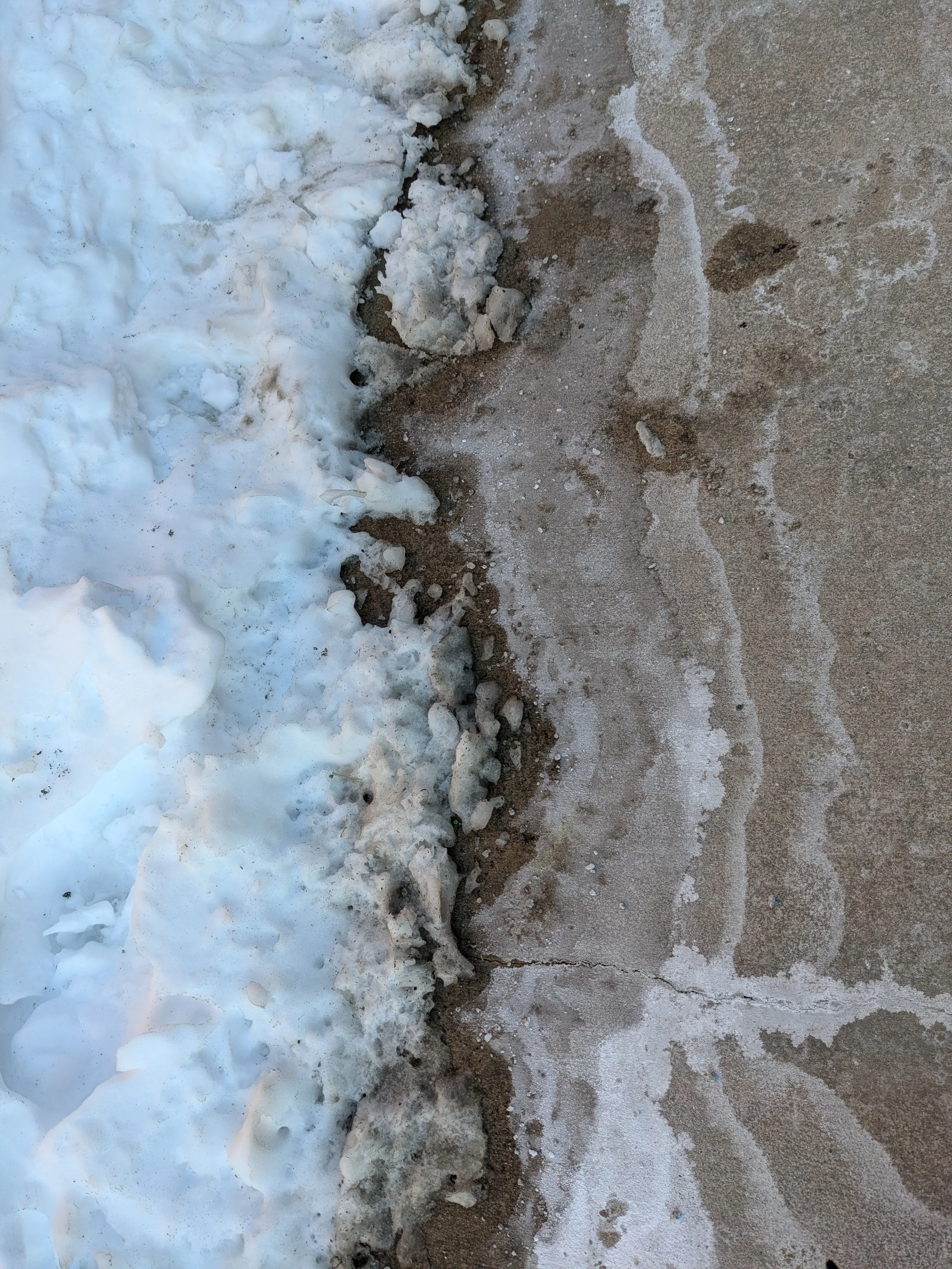 Close-up of a snowbank with melting snow and ice mixed with dirt, slush, and sand on a sidewalk.