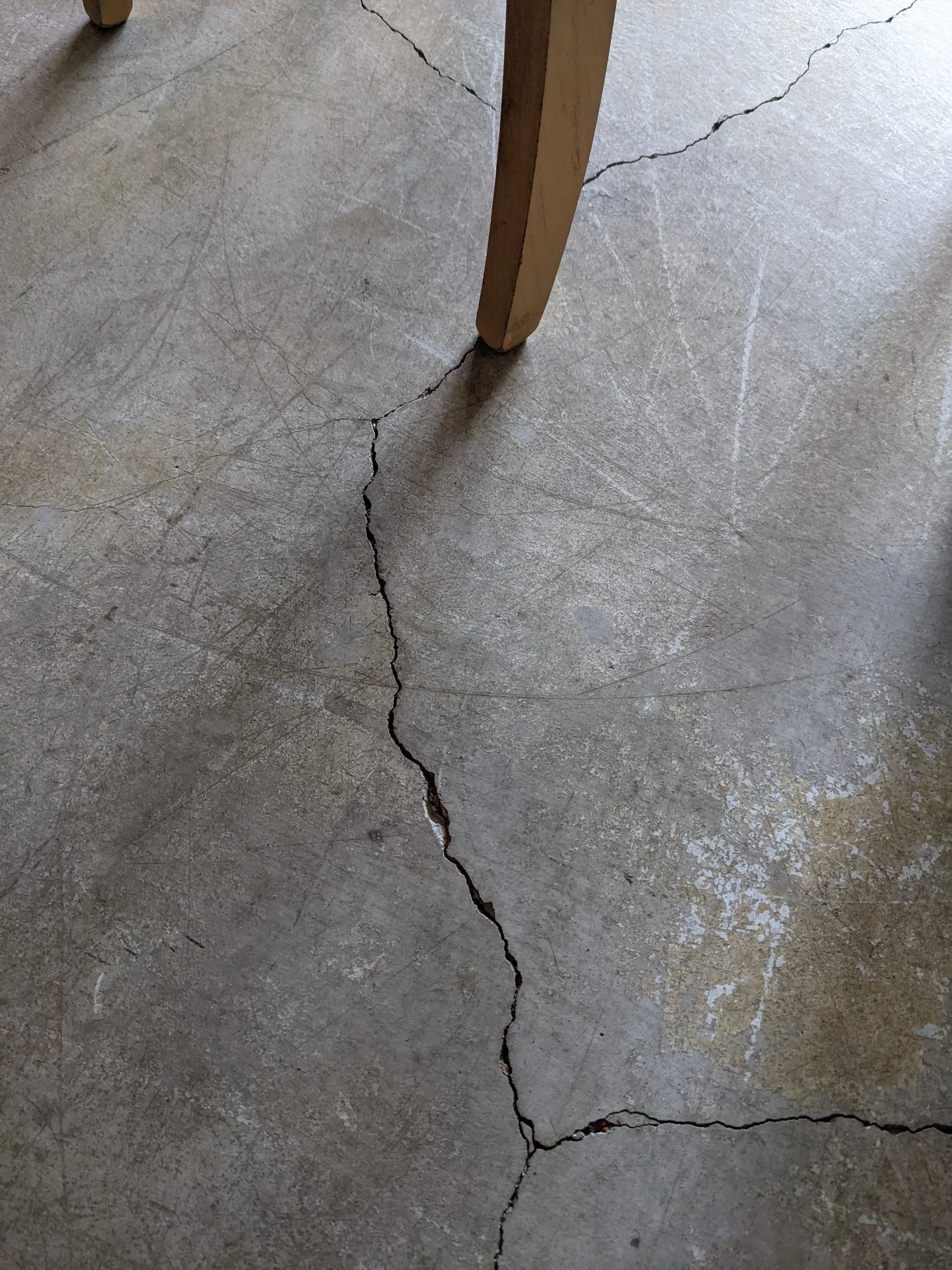Cracked concrete floor beneath a wooden table leg.