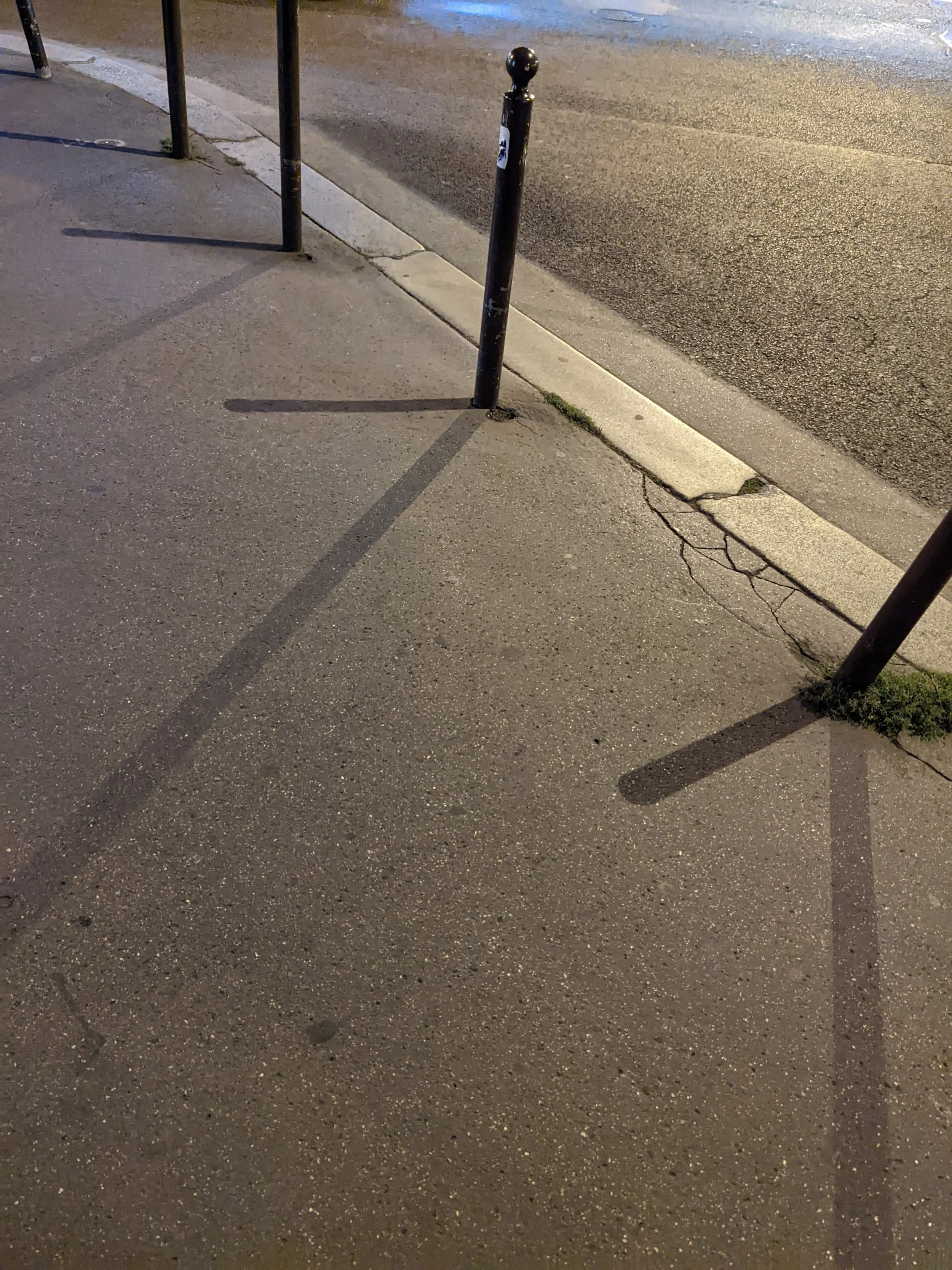 Street corner with two black metal posts casting long shadows on the sidewalk at night.
