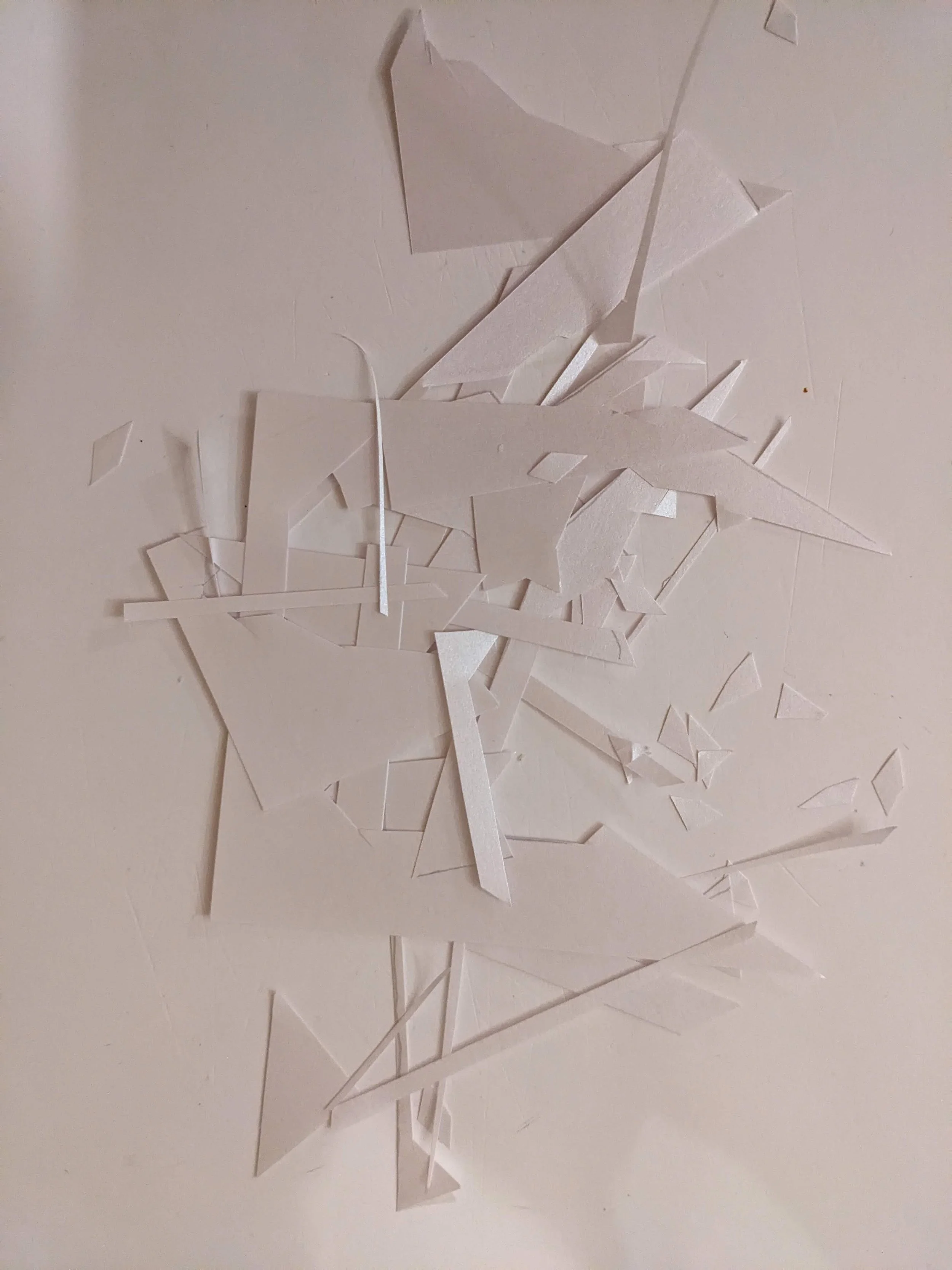 A collection of small, white, angular paper pieces scattered on a light-colored surface.