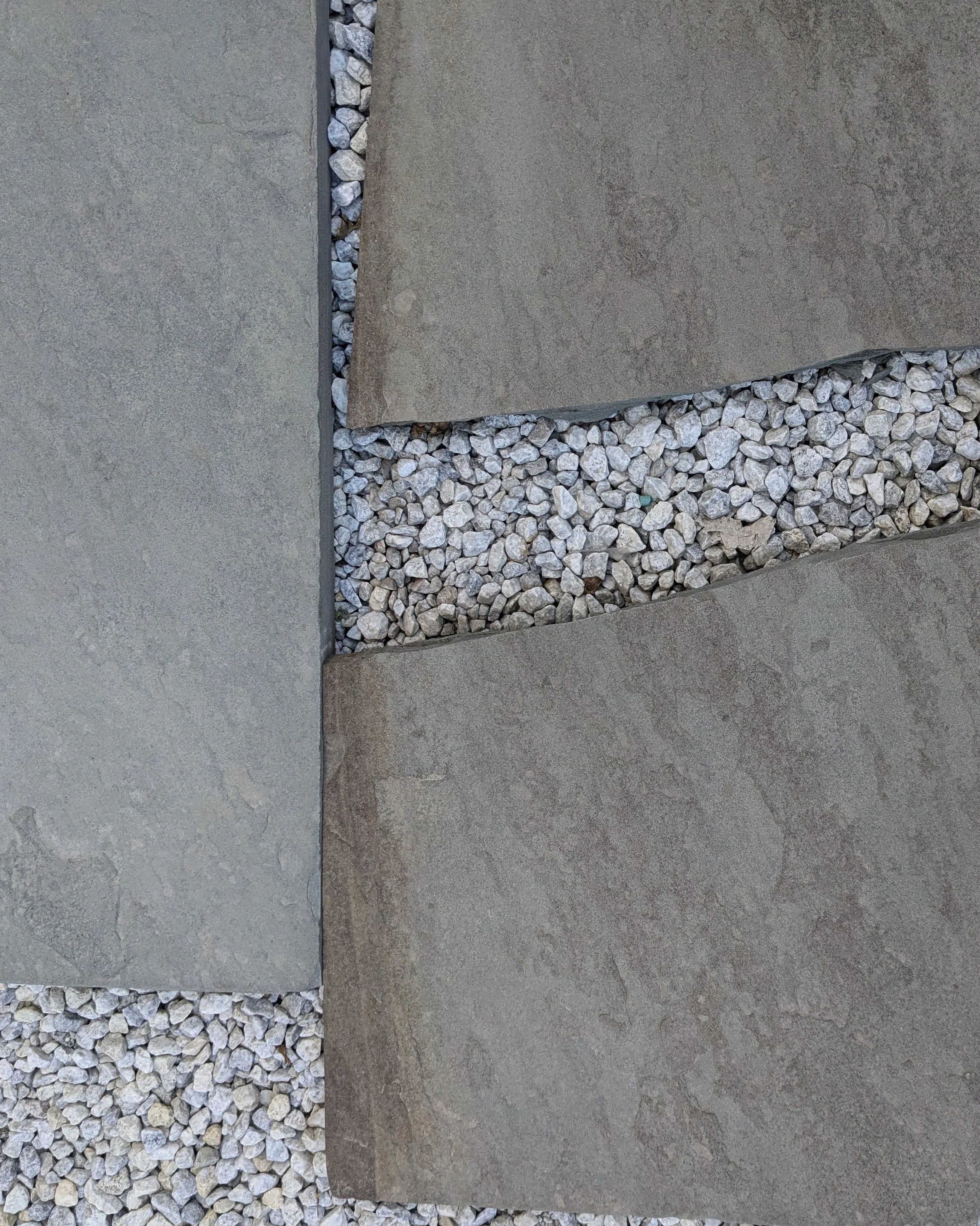 Close-up of concrete pavers with a narrow strip of small white rocks between them.