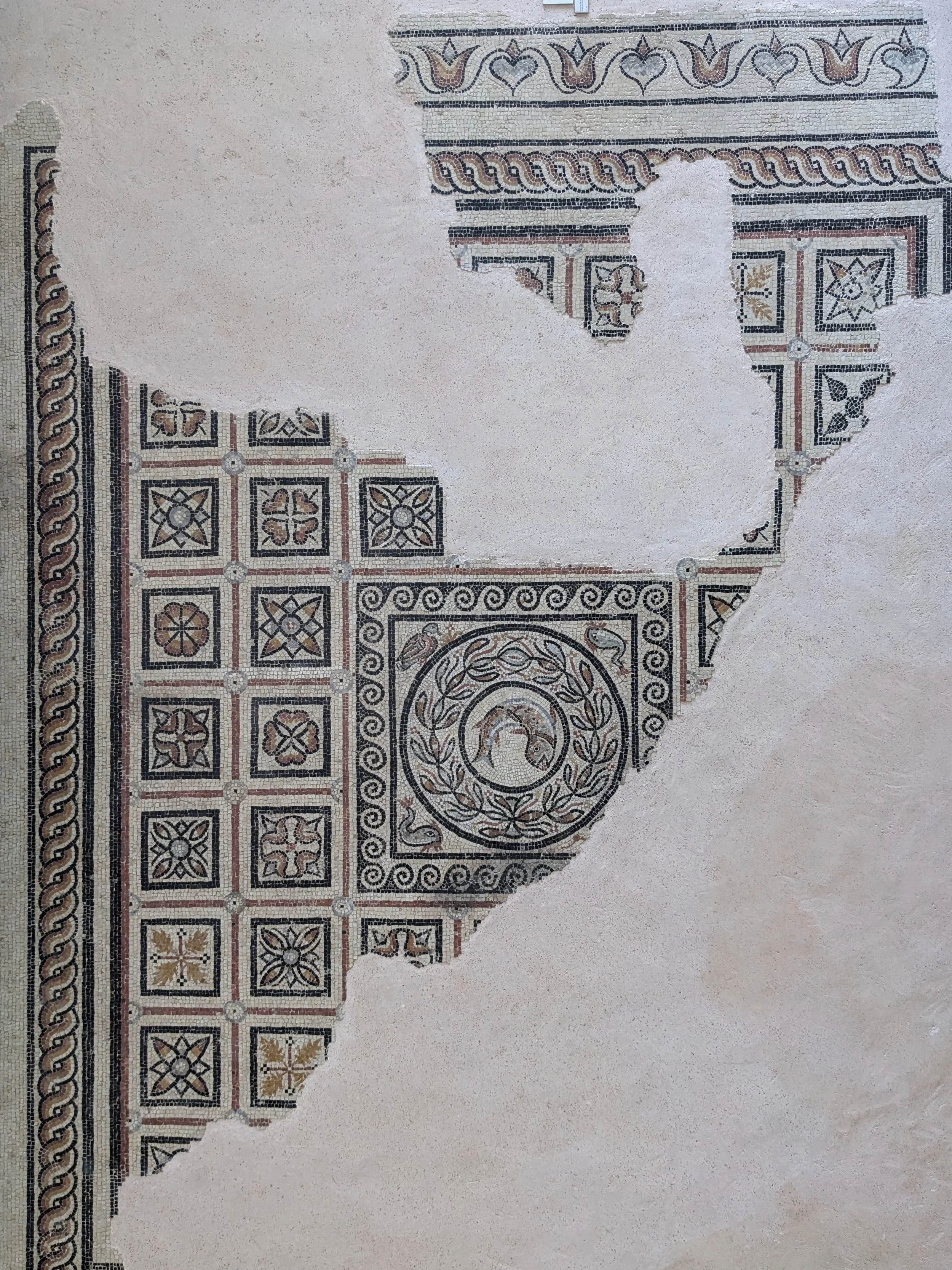 Restored ancient mosaic with geometric and floral patterns, featuring a circular design with a bird motif, and decorative borders.