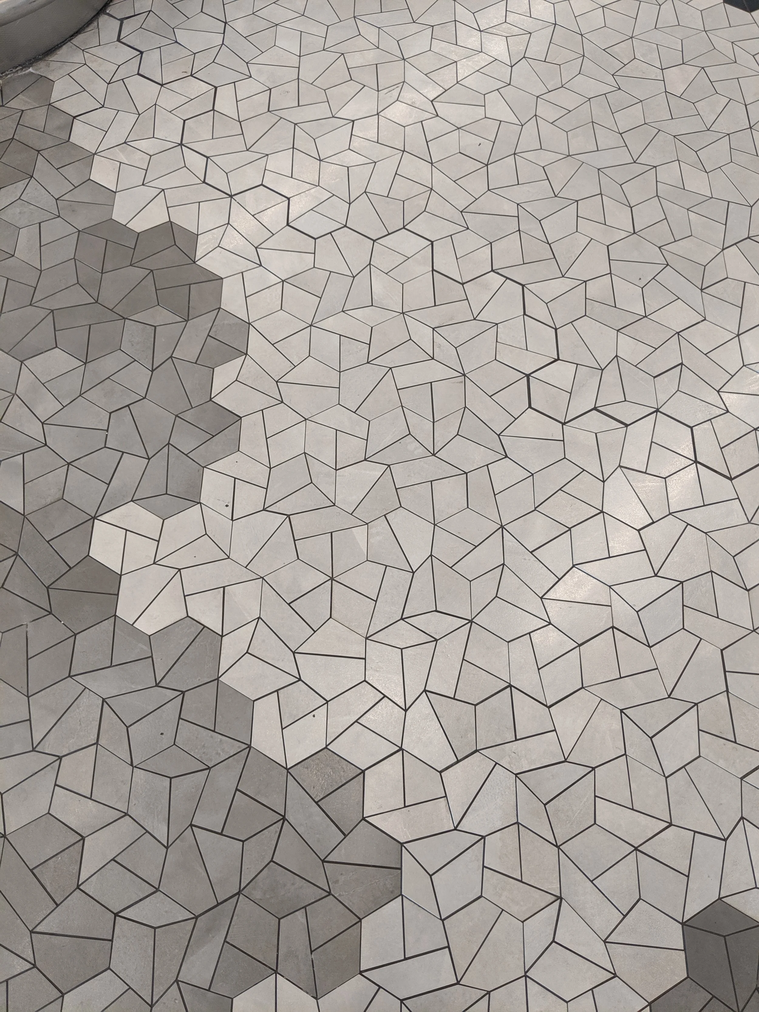 Floor with a geometric tile pattern consisting of hexagons and irregular polygons, outlined in black, in a light gray color.