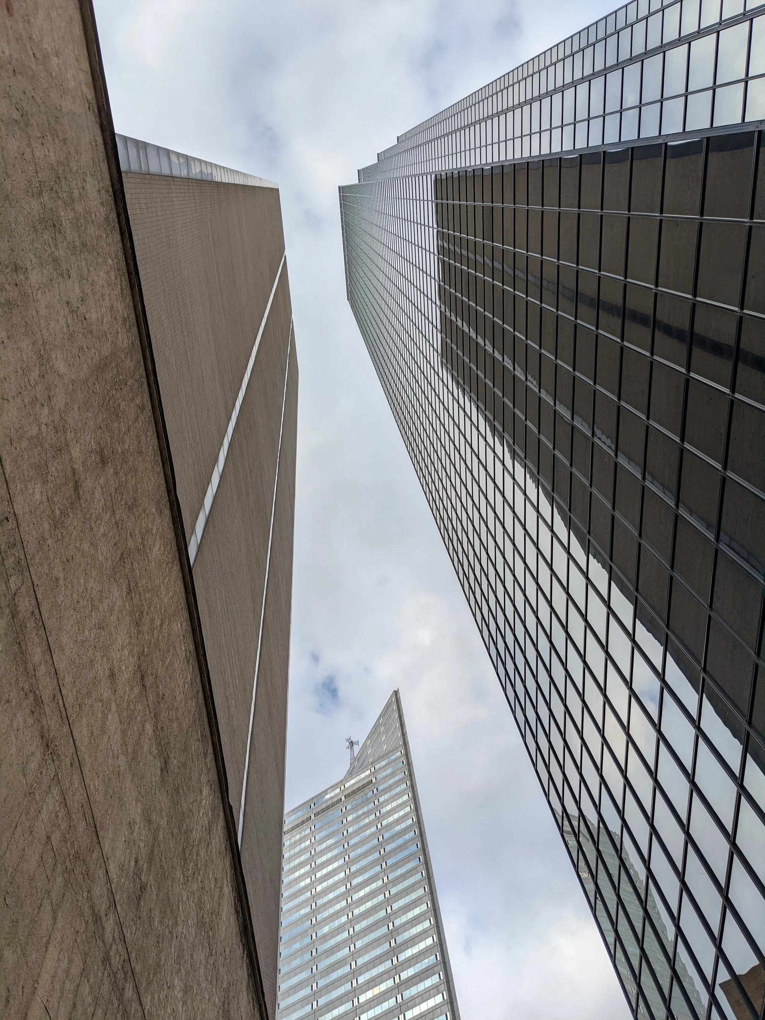 Looking up at multiple tall modern skyscraper buildings in a city, with the sky visible at the top of the image.