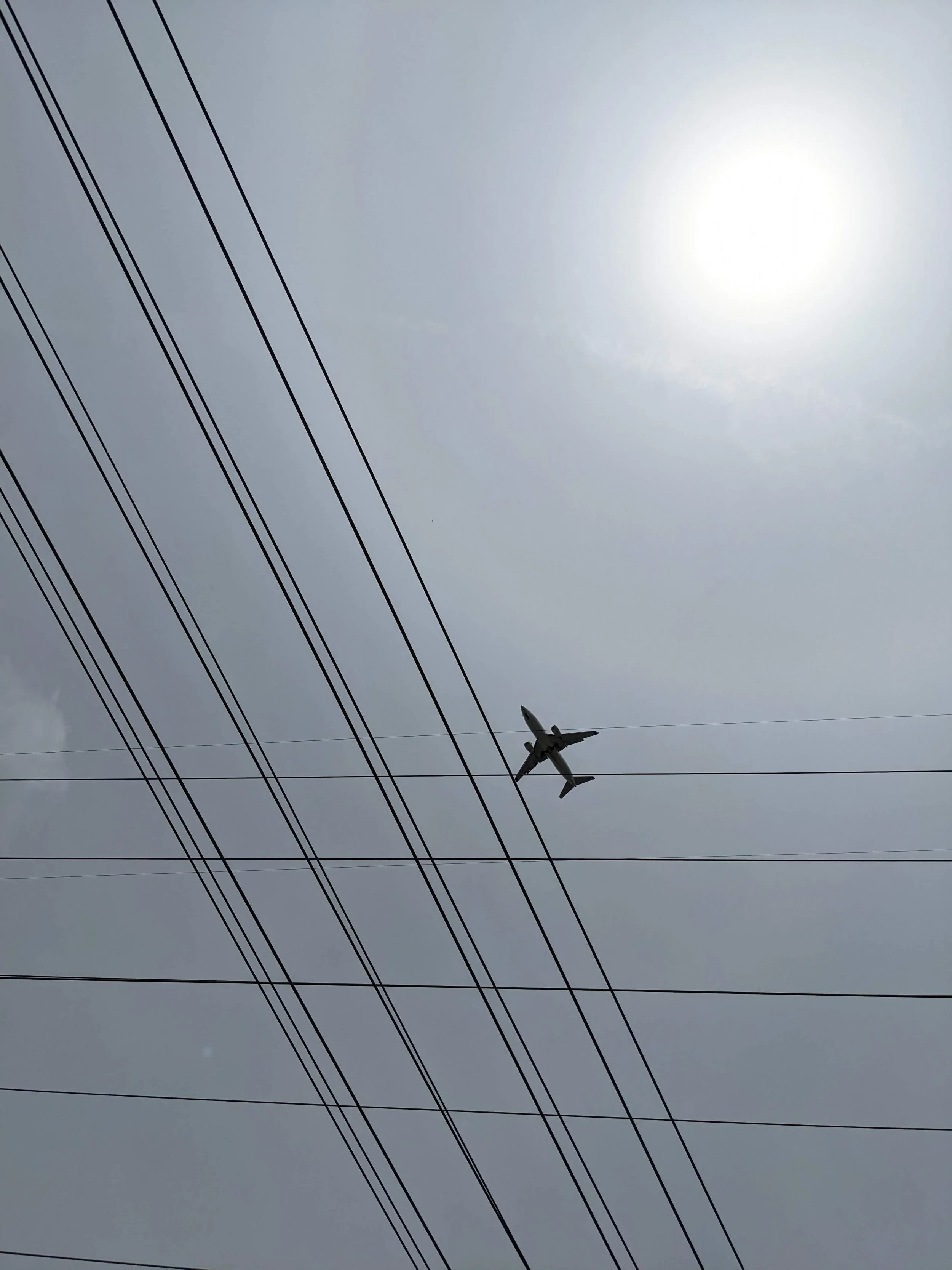 An airplane flying in the sky near electrical power lines during daytime with a cloudy sky.