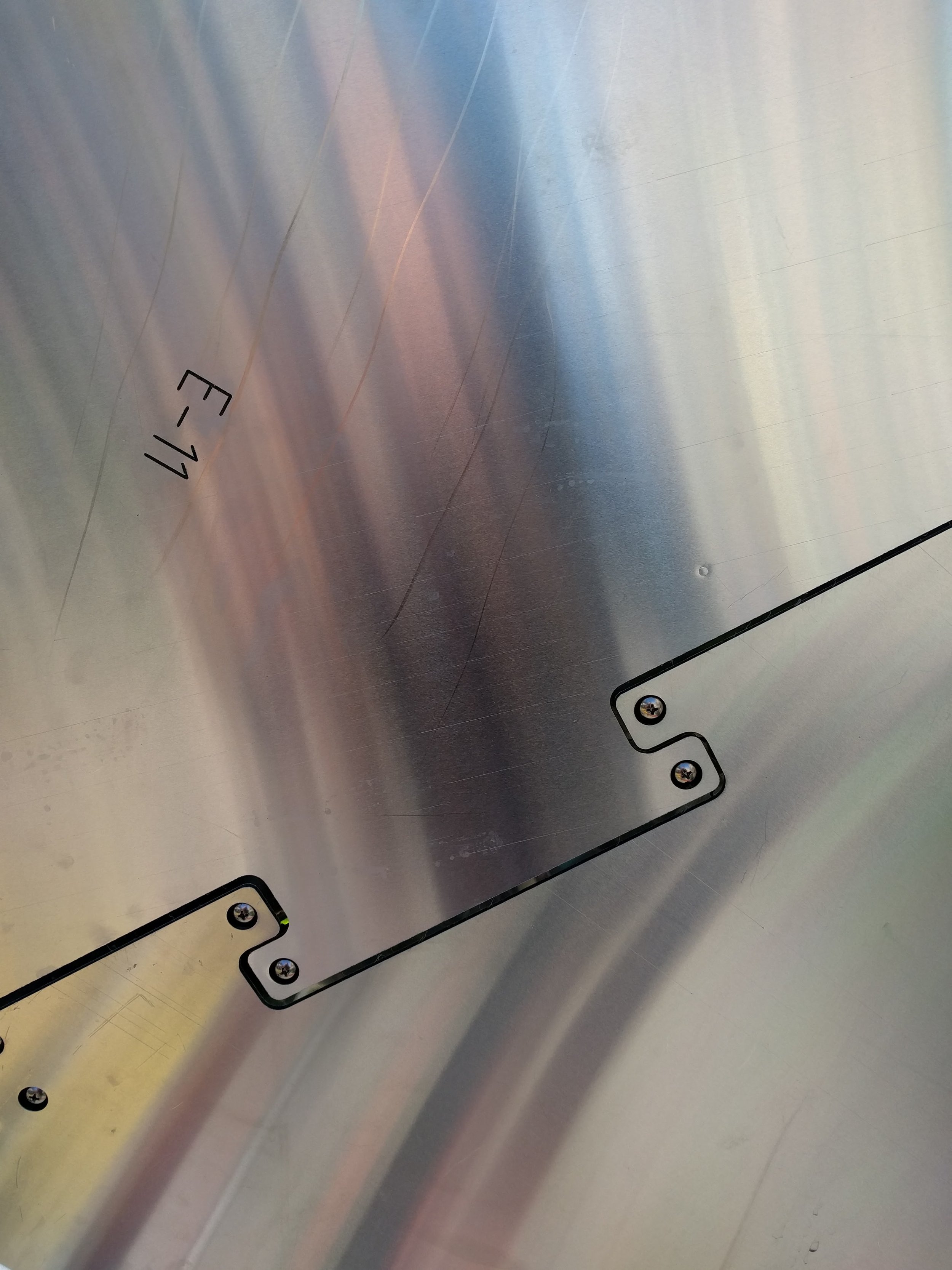 Close-up of a metallic surface with engraved text and a small black outline of a rectangle with four screws.