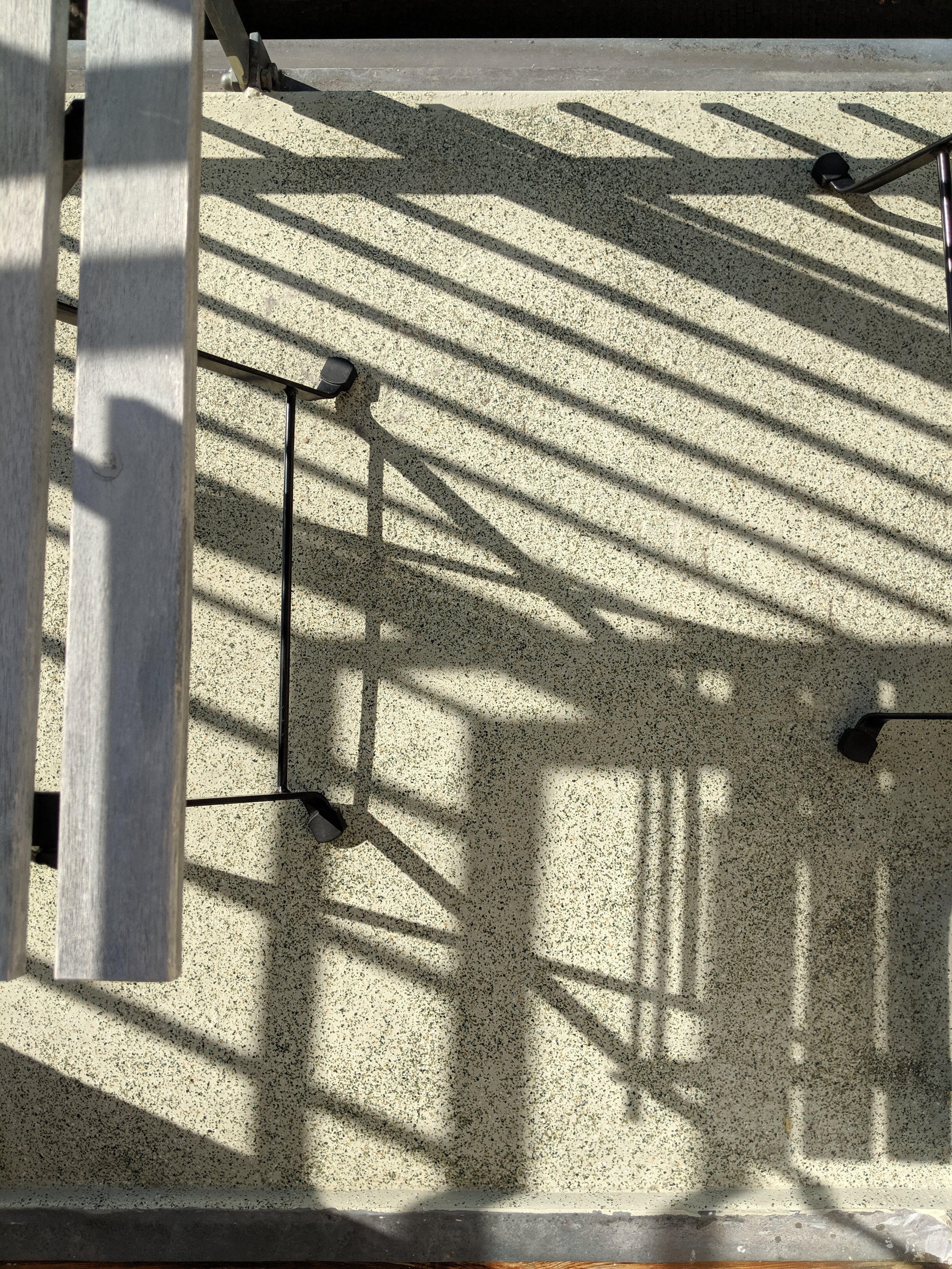 Shadows of metal railing cast on a textured concrete or terrazzo floor, with parts of the railing visible in the frame.