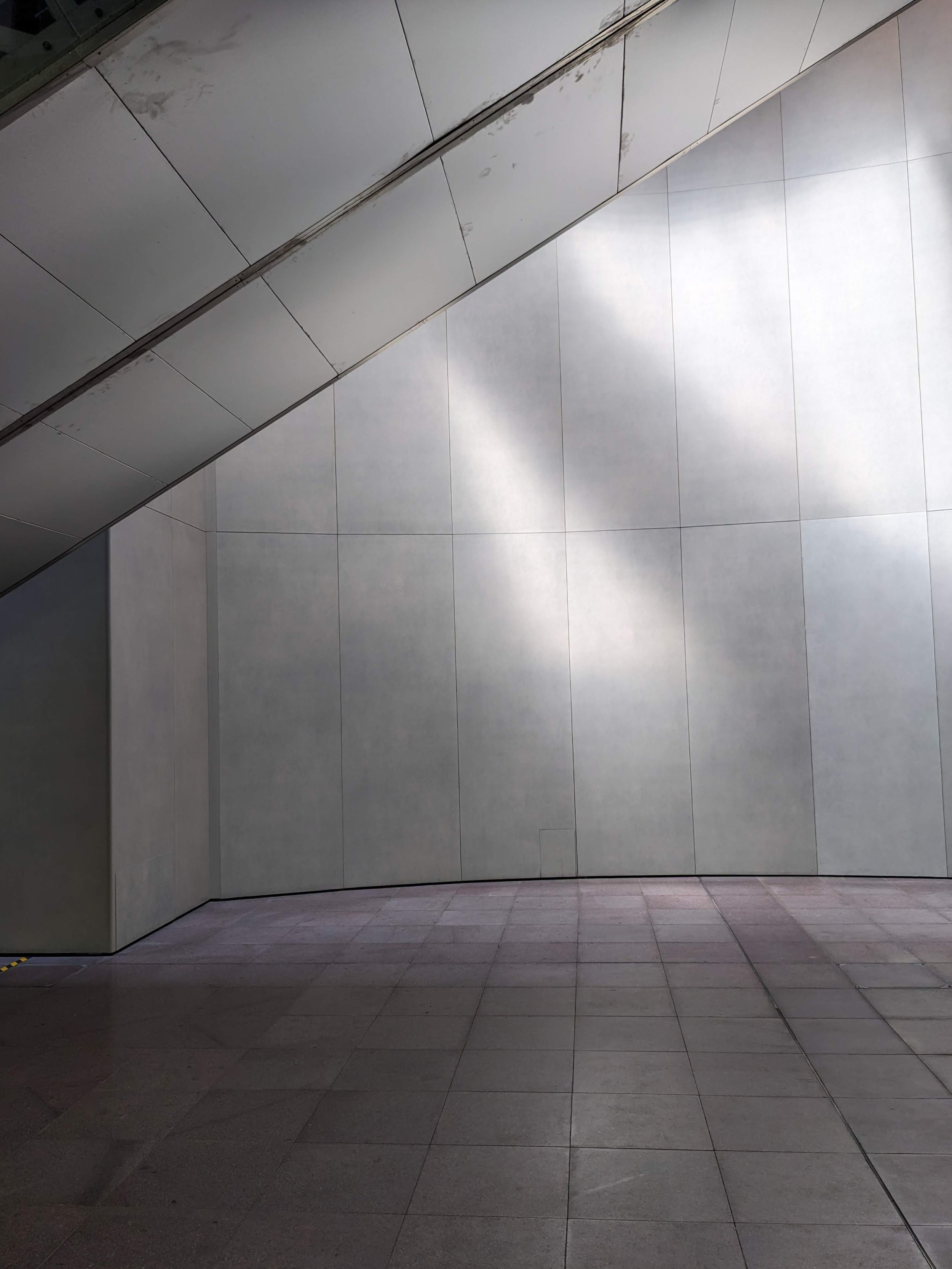 Empty modern hallway with tiled walls and floor, metallic panel on the wall, and subtle reflection of light.