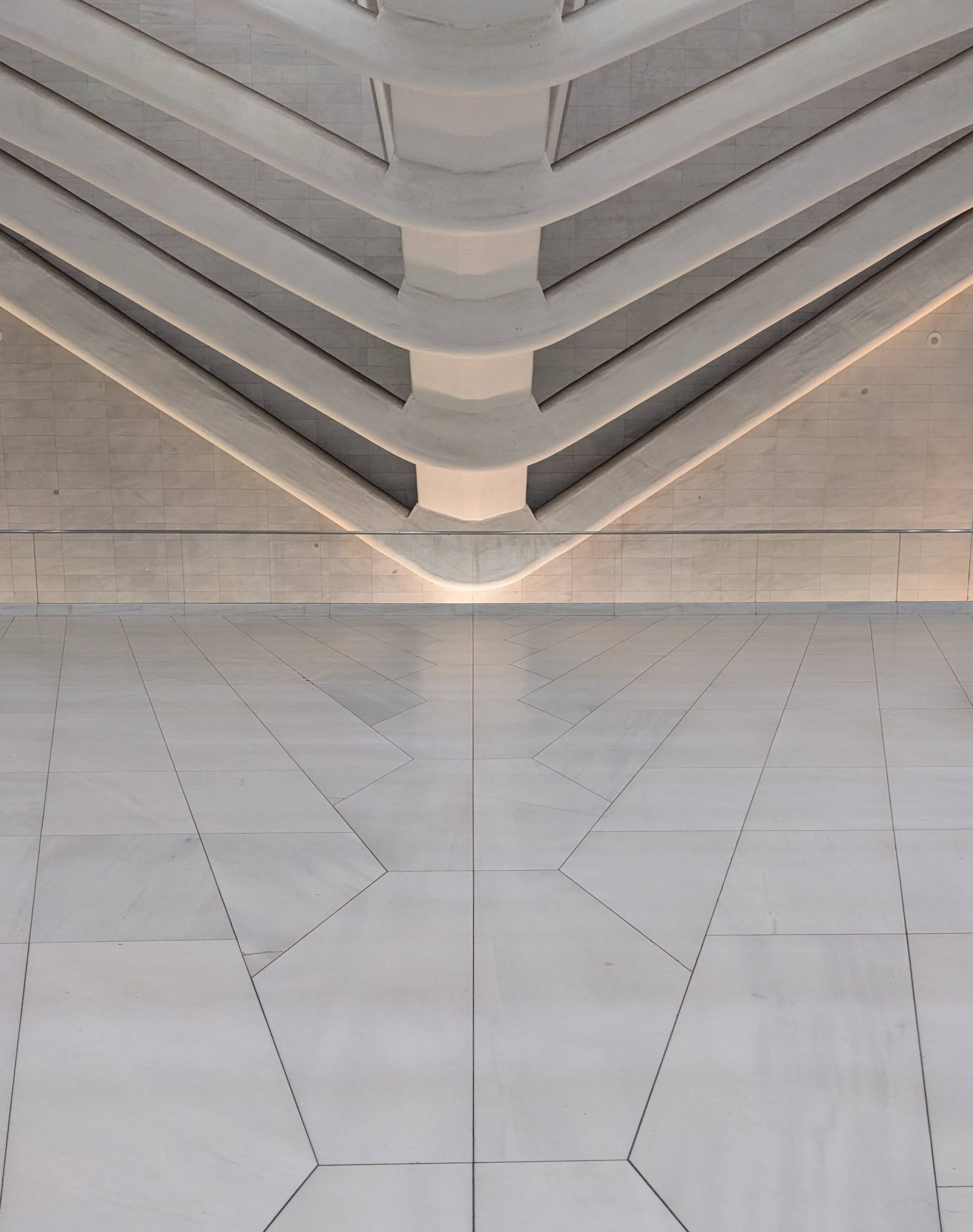 Looking down at a symmetrical staircase with white marble steps and beige tiled floor.