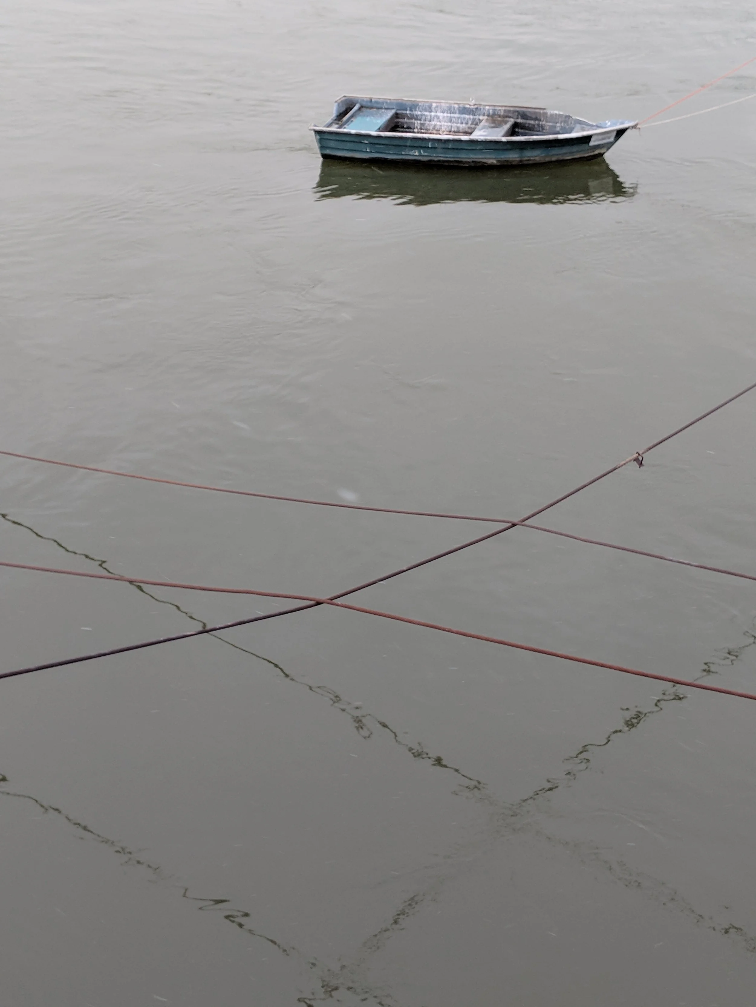 A small boat floating on water, tethered to a thin pink rope, with the boat's reflection visible on the water's surface.