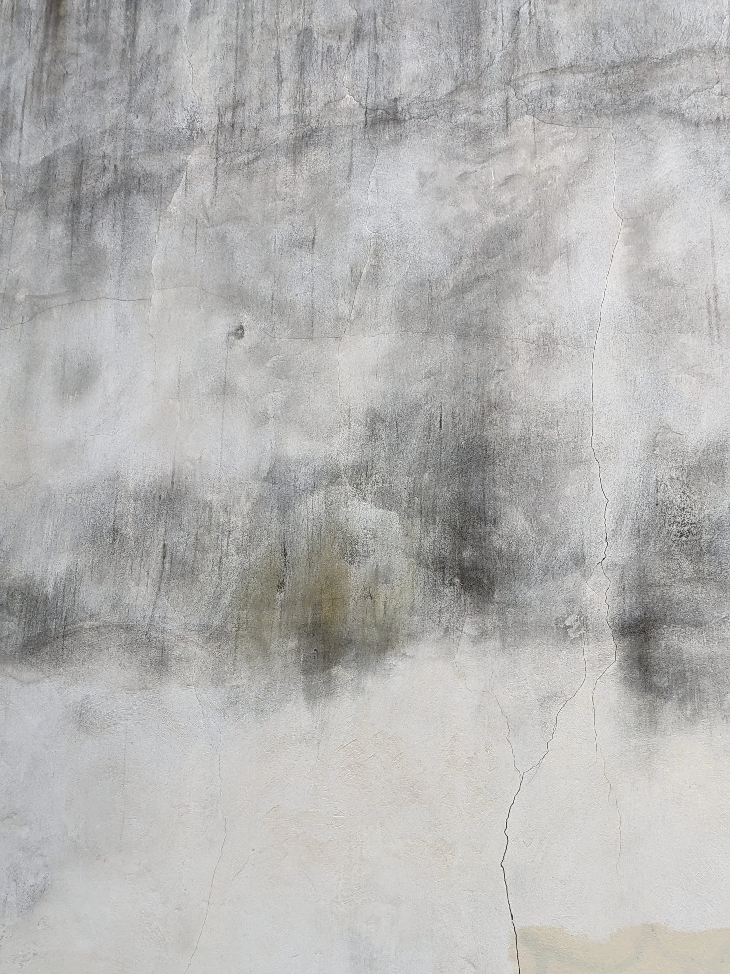 A weathered and cracked concrete wall with various shades of gray and some light beige areas.