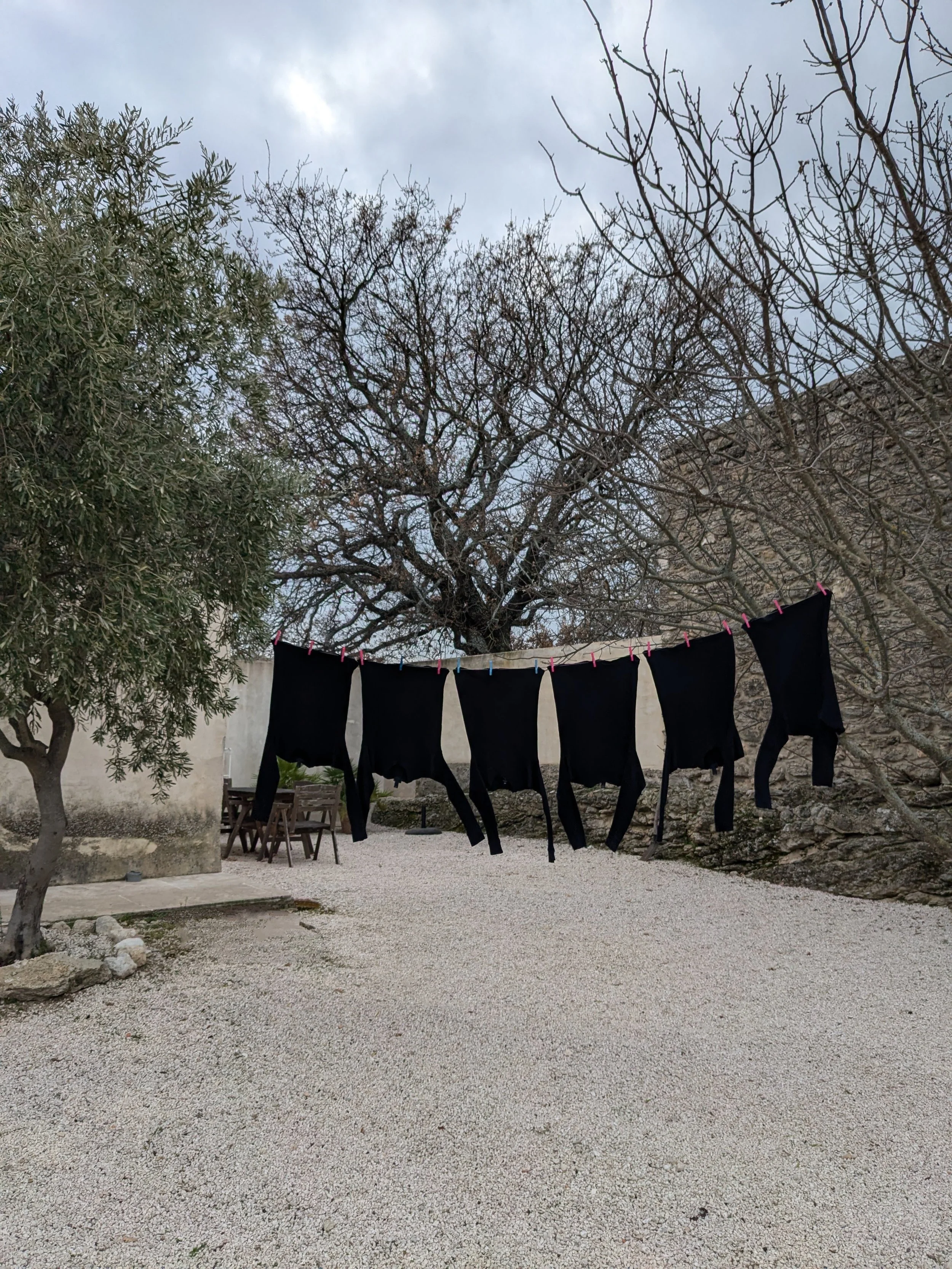 Black shirts hanging on a line outdoors with trees and a stone wall in the background.