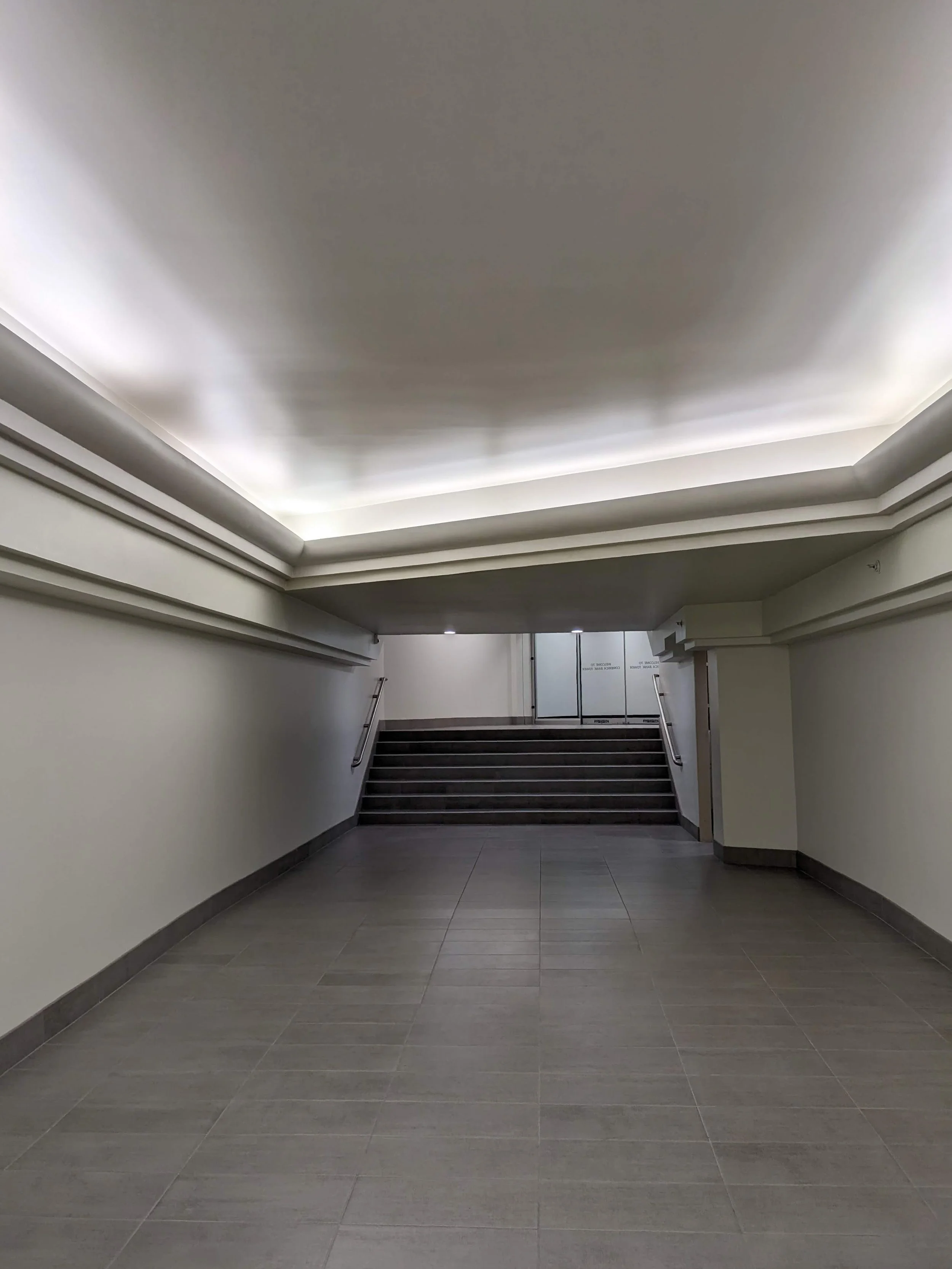 An interior stairway with tiled flooring, walls painted light, a ceiling with built-in lighting and layered crown molding, and glass doors at the top of the stairs.