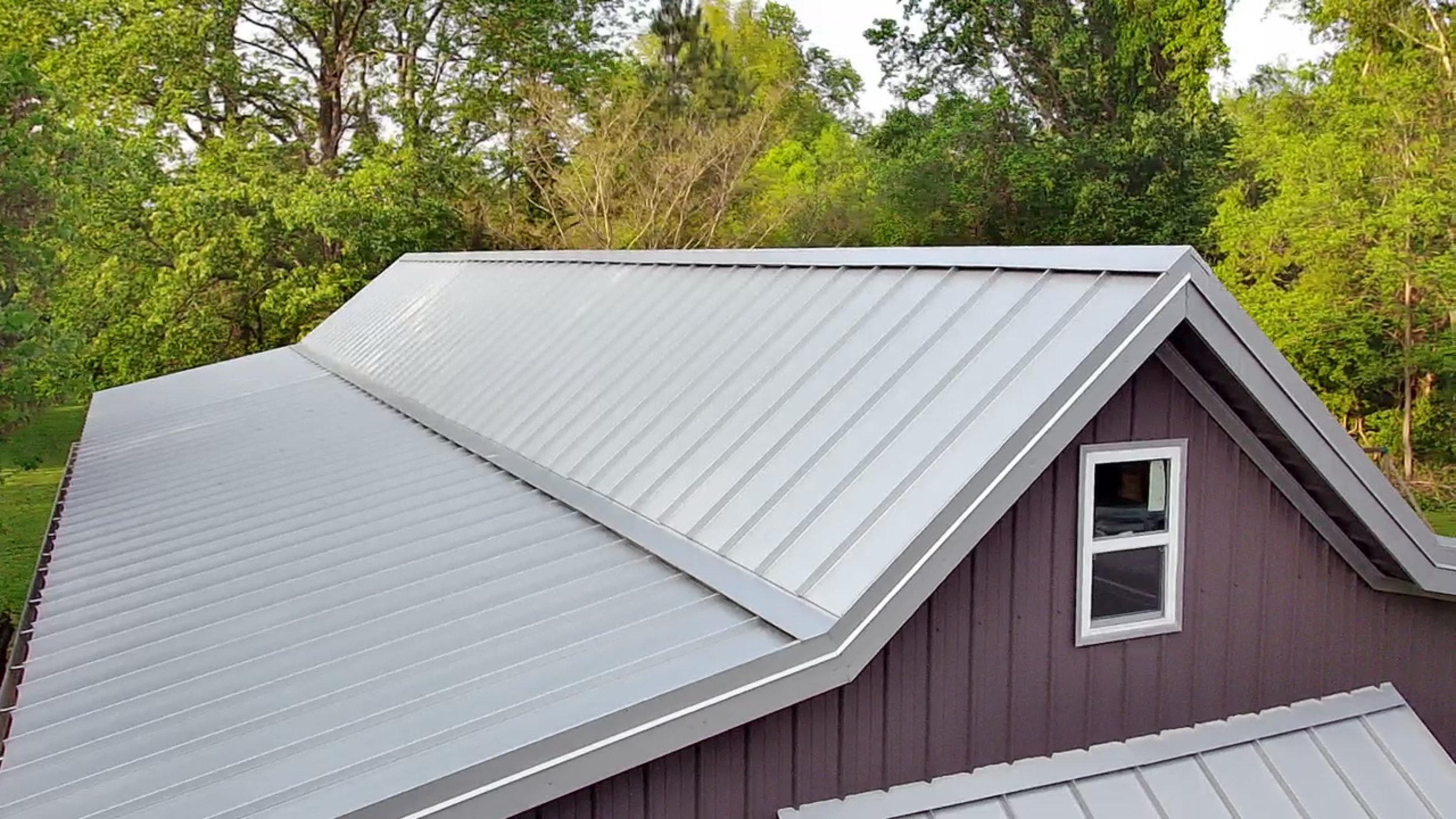 A house with a metal roof and purple siding, surrounded by green trees.