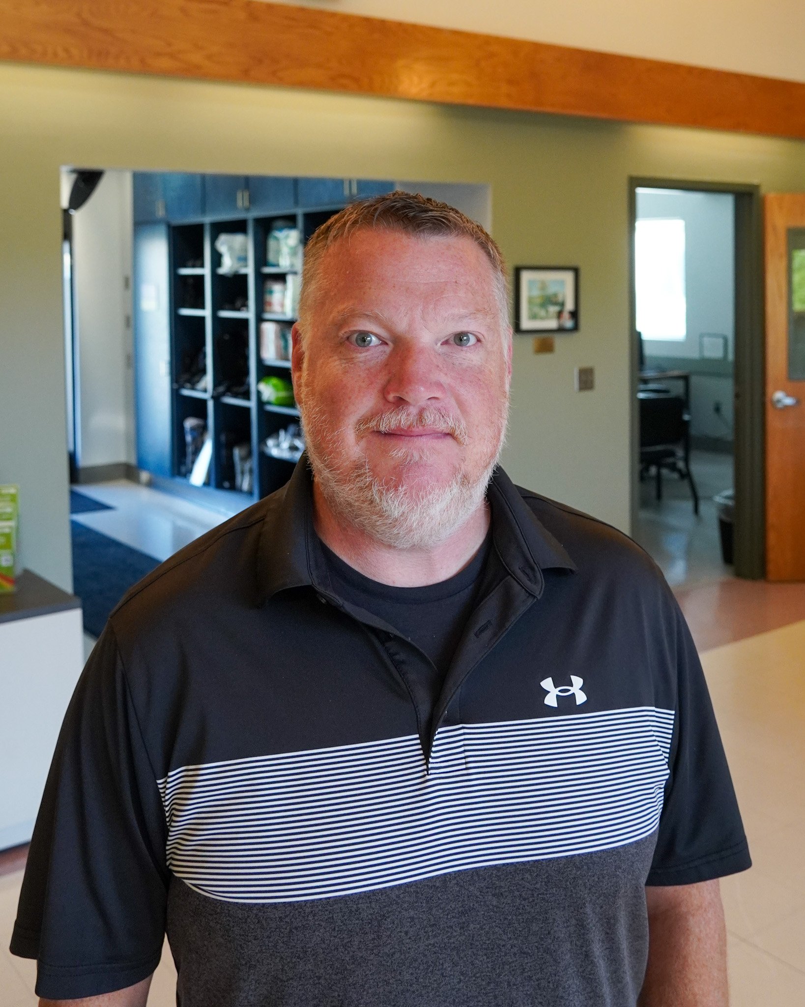 photo of brian slight smile, gray hair, facial hair, with a lobby setting behind him
