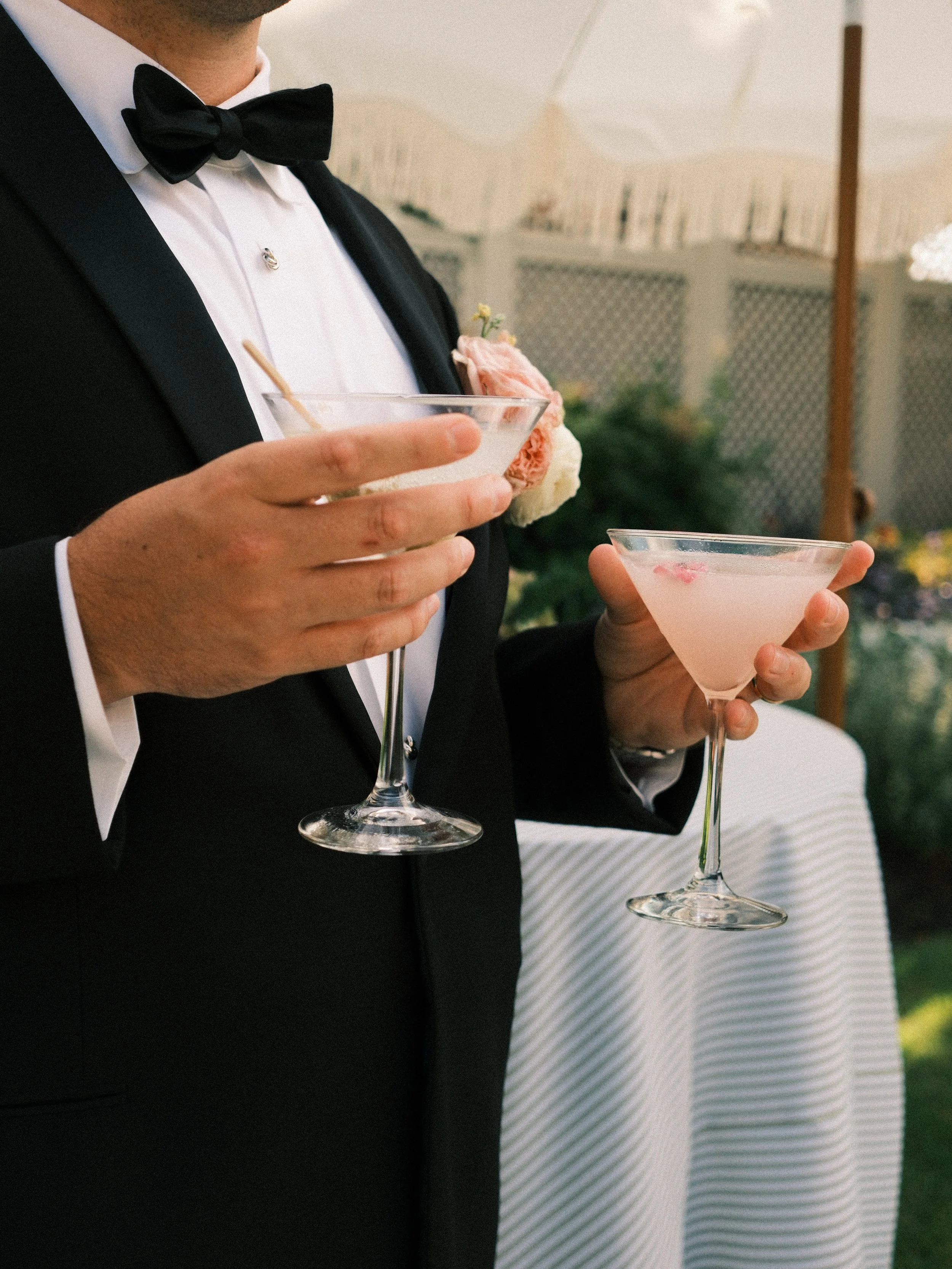 Two people in formal attire holding cocktail glasses at an outdoor event.