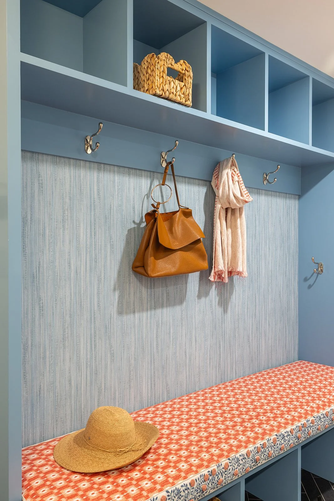Mudroom bench with coral and blue floral tape trim under a blue grasscloth wall and polished nickel double hooks