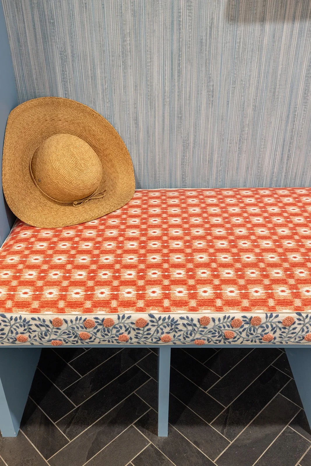 Close-up of a coral geometric bench cushion finished with blue and coral floral tape over slate herringbone tile