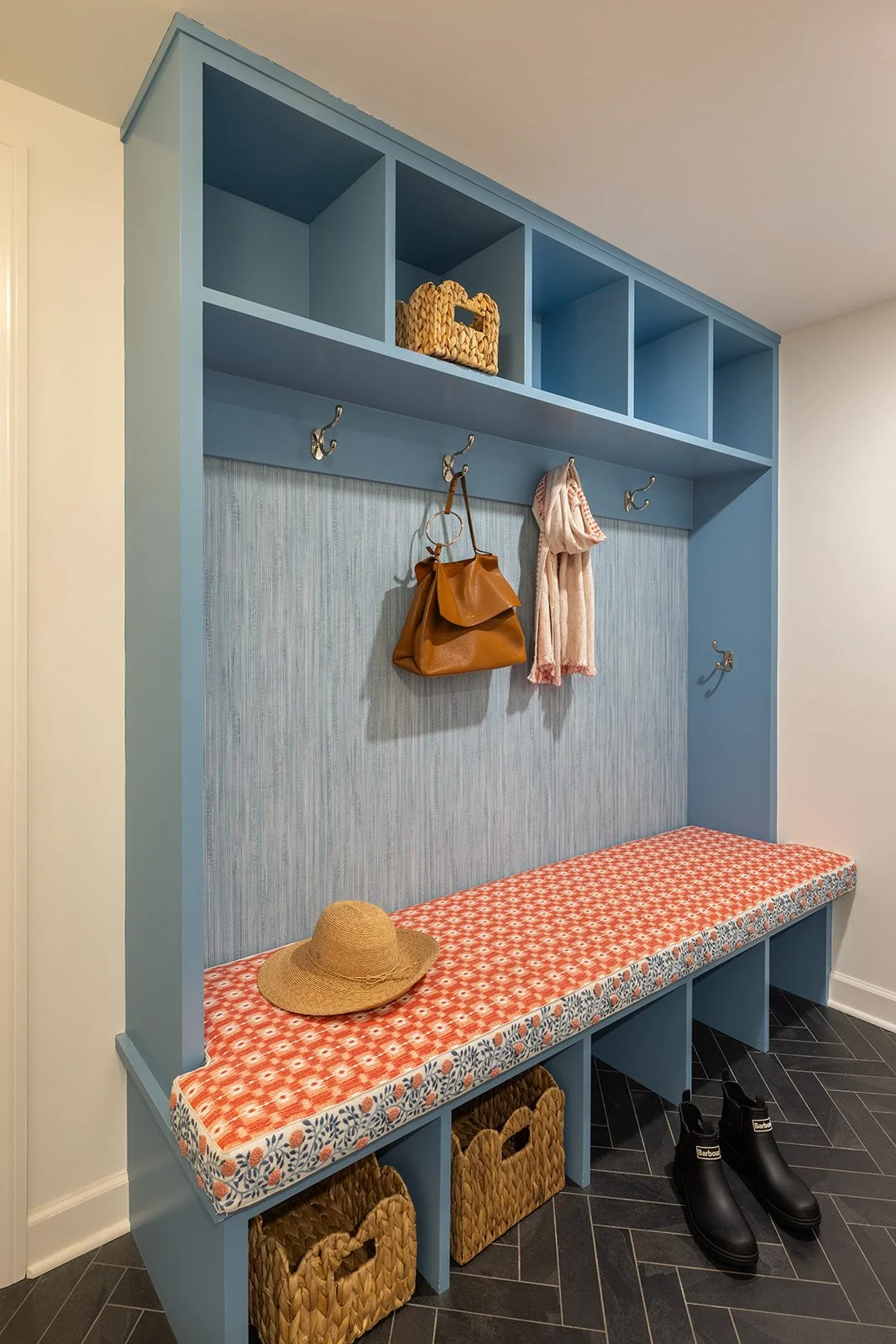 Chappaqua mudroom with blue-green built-in lockers, canvas storage bins, and a coral patterned bench cushion