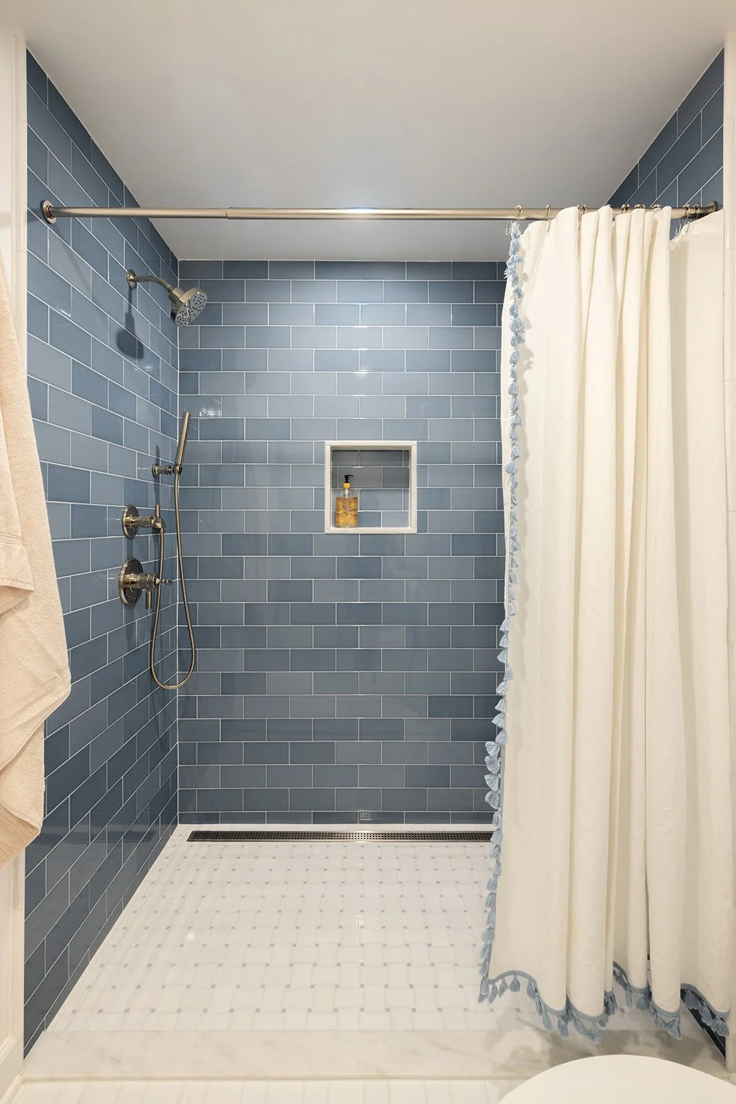 Bathroom shower with blue subway tile walls, a built-in niche with toiletries, a silver shower head, and a white shower curtain with blue trim.