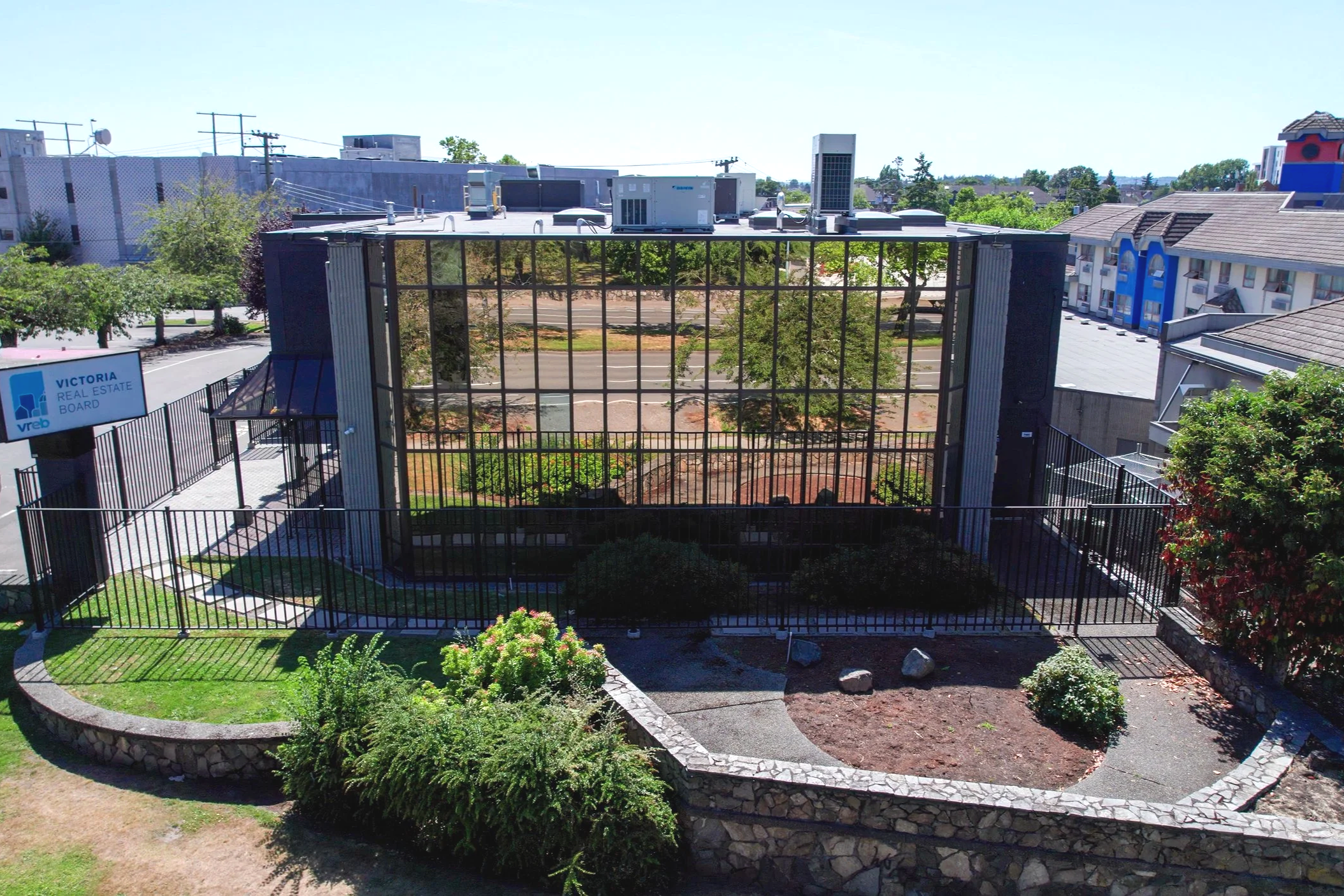 View of a fenced outdoor area with trees and a building backdrop, including a sign reading 'Victoria Real Estate Board'.