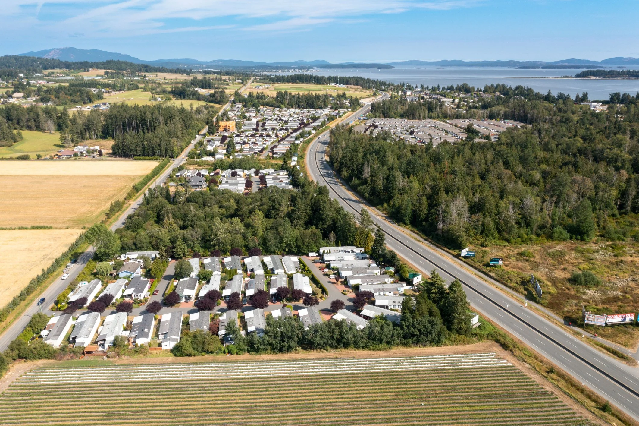 Aerial view of the Saanich Peninsula, with a highway, residential area, farmland, and a body of water in the distance.