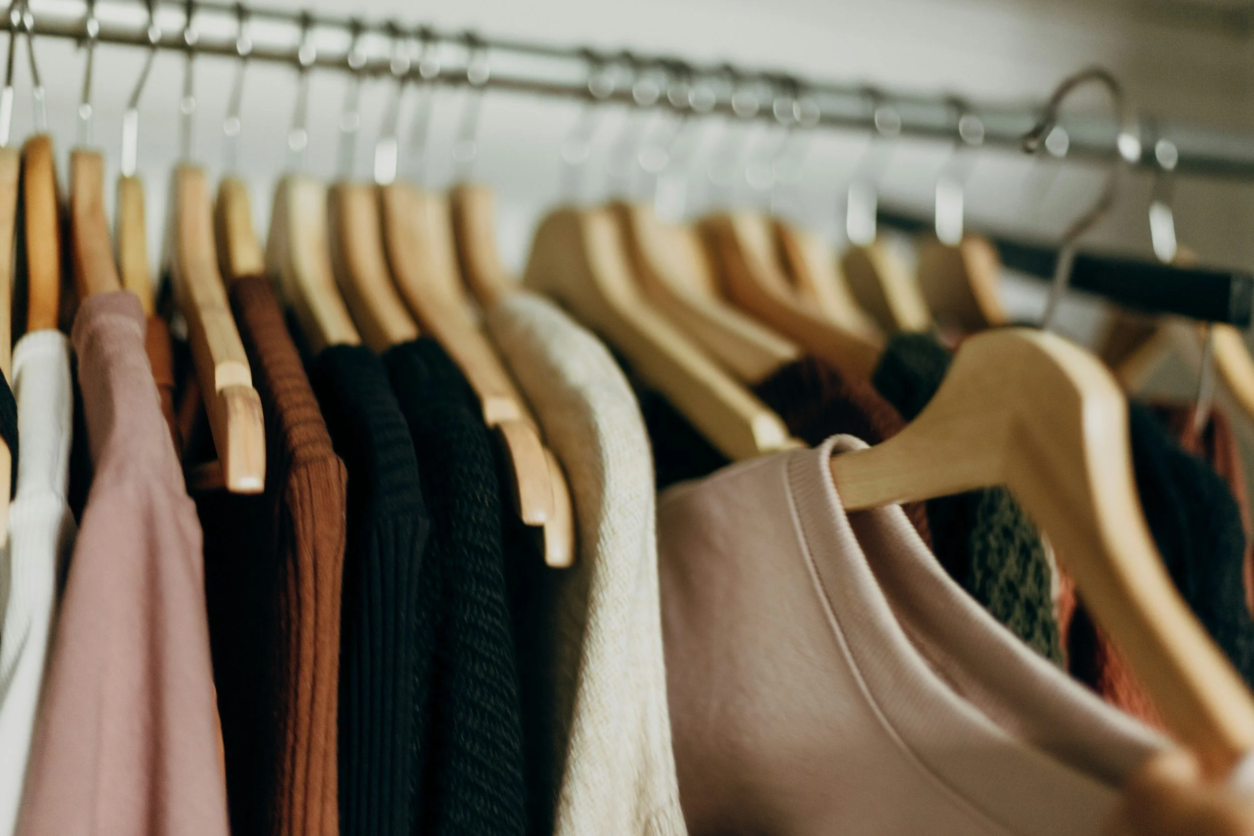 Clothing items hanging on a closet rod, including sweaters, jackets, and shirts on wooden hangers.
