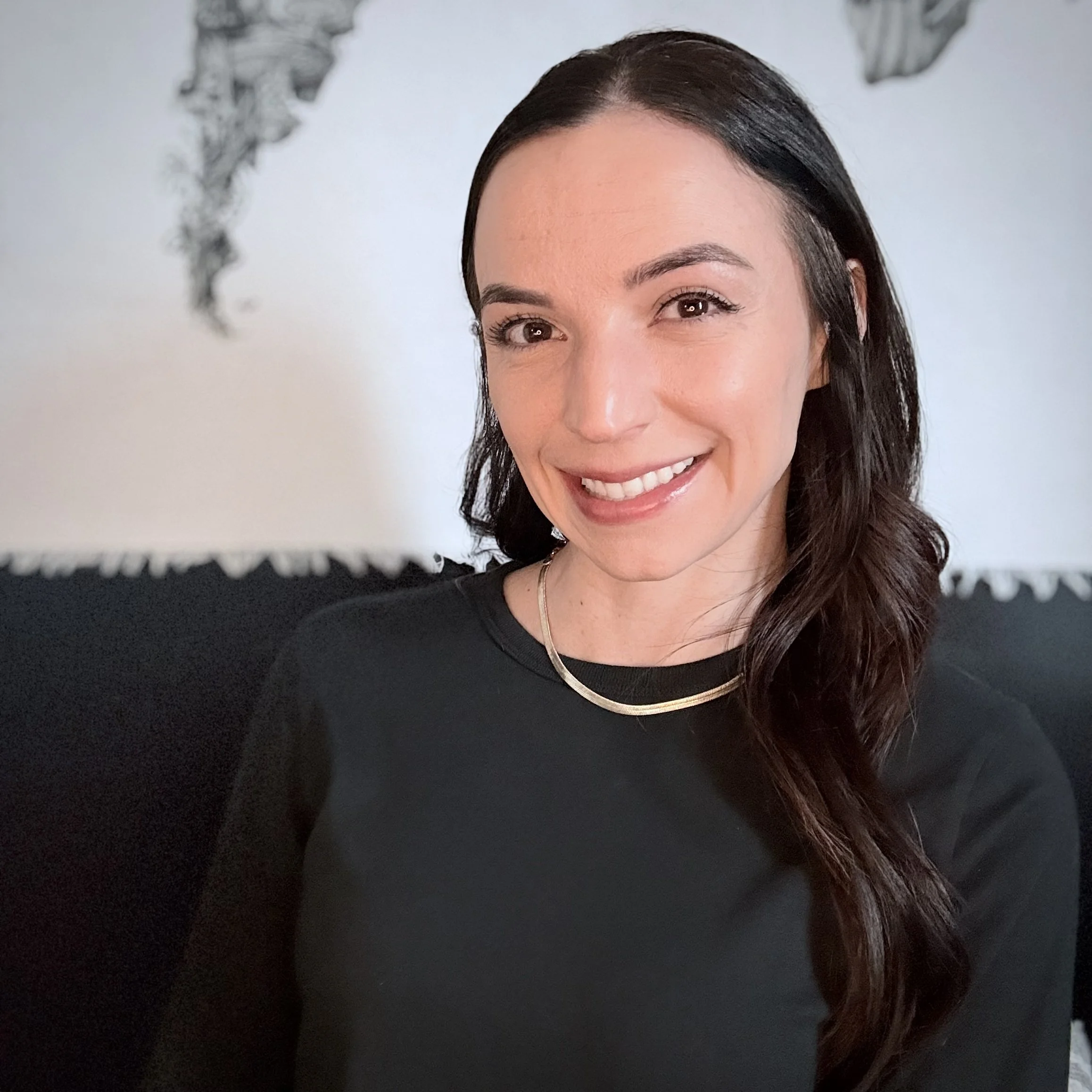 A woman with long dark hair wearing a black top and jewelry, smiling in front of a light background featuring a world map illustration.