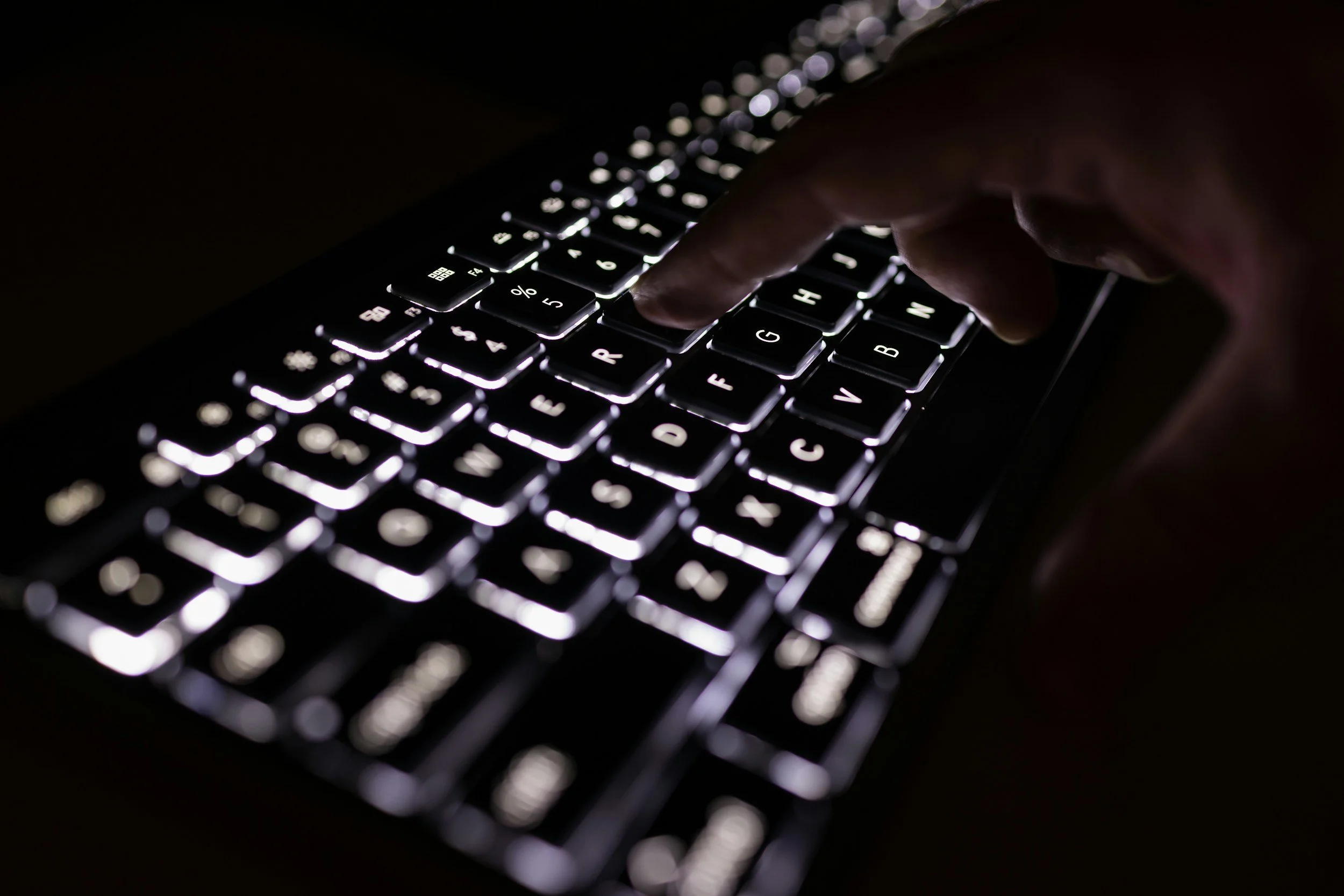 A person typing on a backlit keyboard in a dark environment.