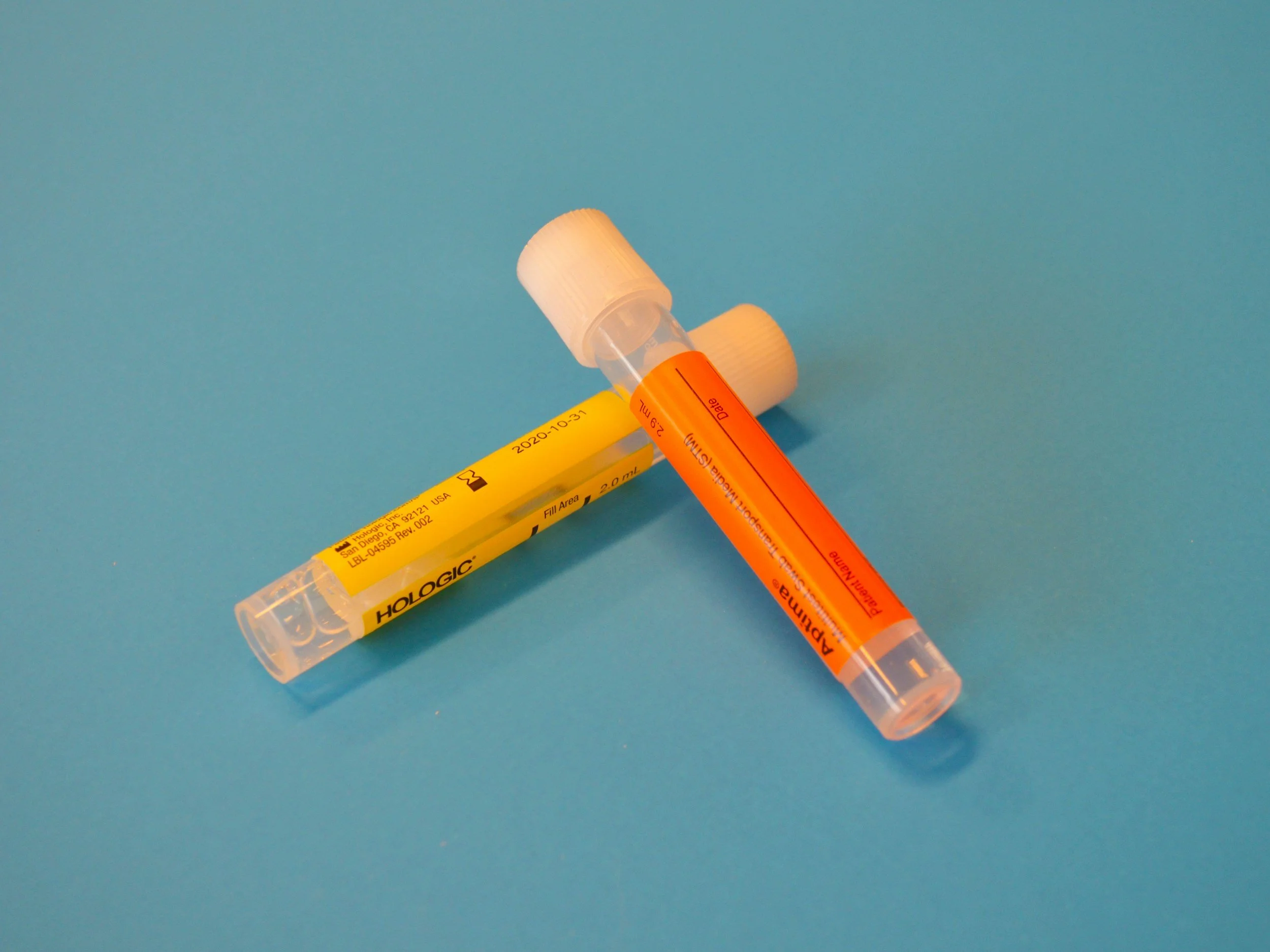 Two urine sample collection tubes with white caps, one yellow labeled 'Hologic' and the other orange labeled 'ARUP', on a blue background.