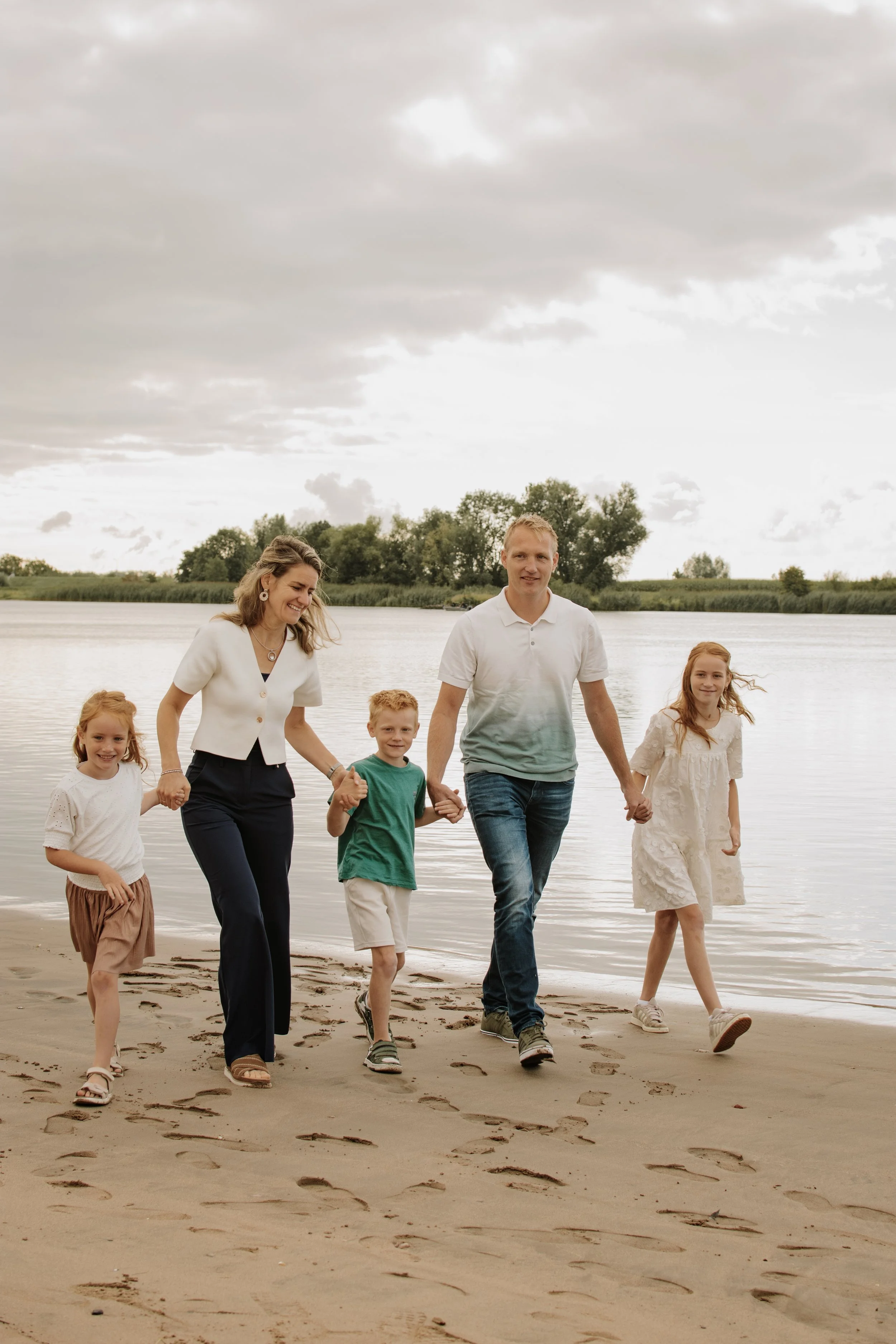 Families die samen hand in hand bij de rivier lopen op het strand, terwijl ze genieten van een mooie dag buiten.