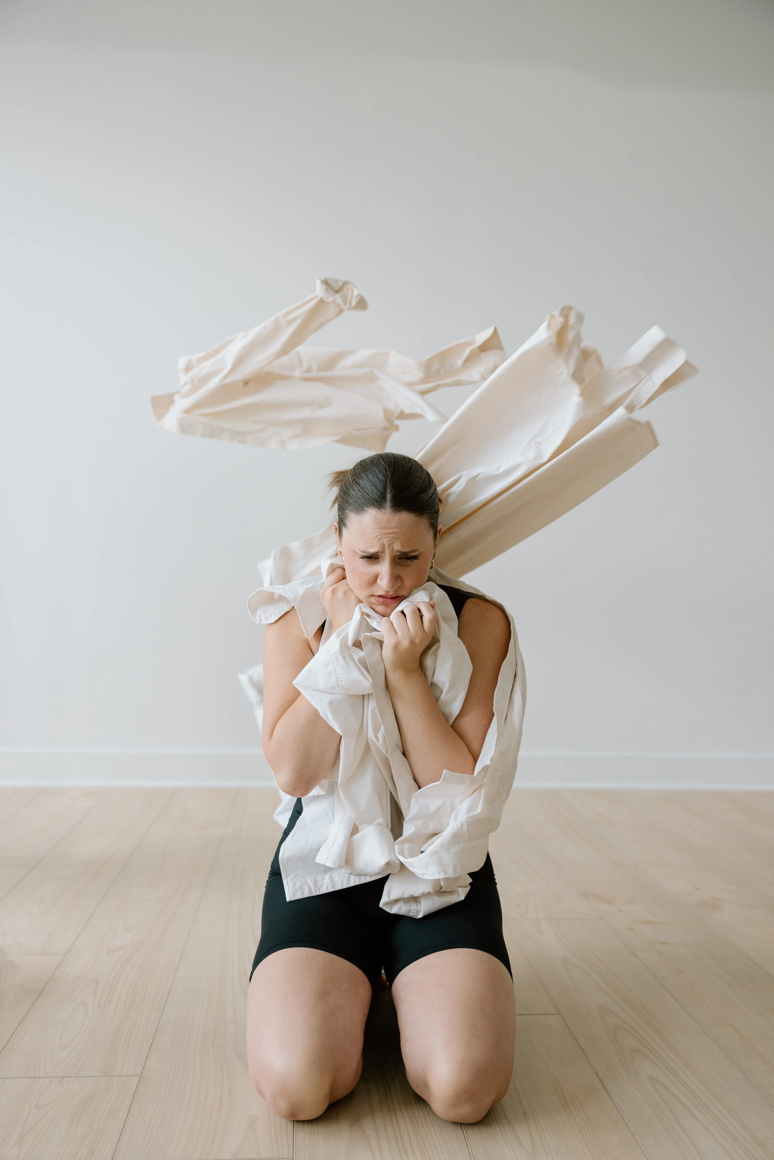 A woman kneeling on the floor, holding fabric and looking distressed, with crumpled fabric flying behind her.