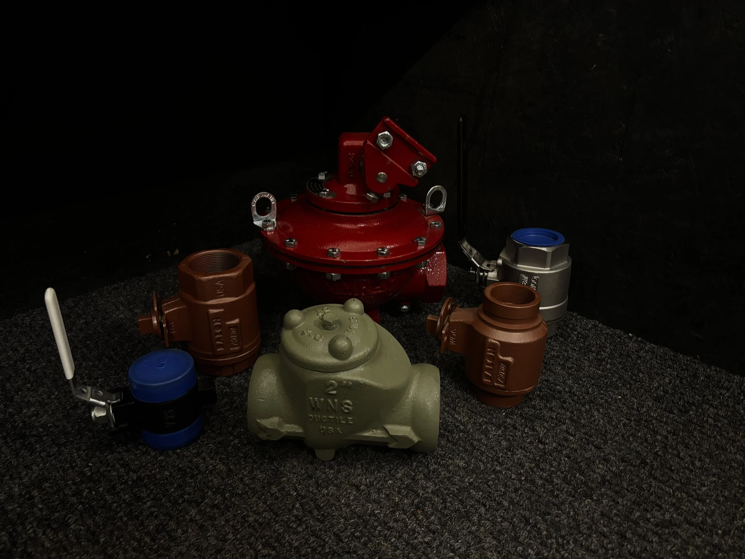 Collection of fire hydrant valves and parts on dark carpeted floor against black wall.