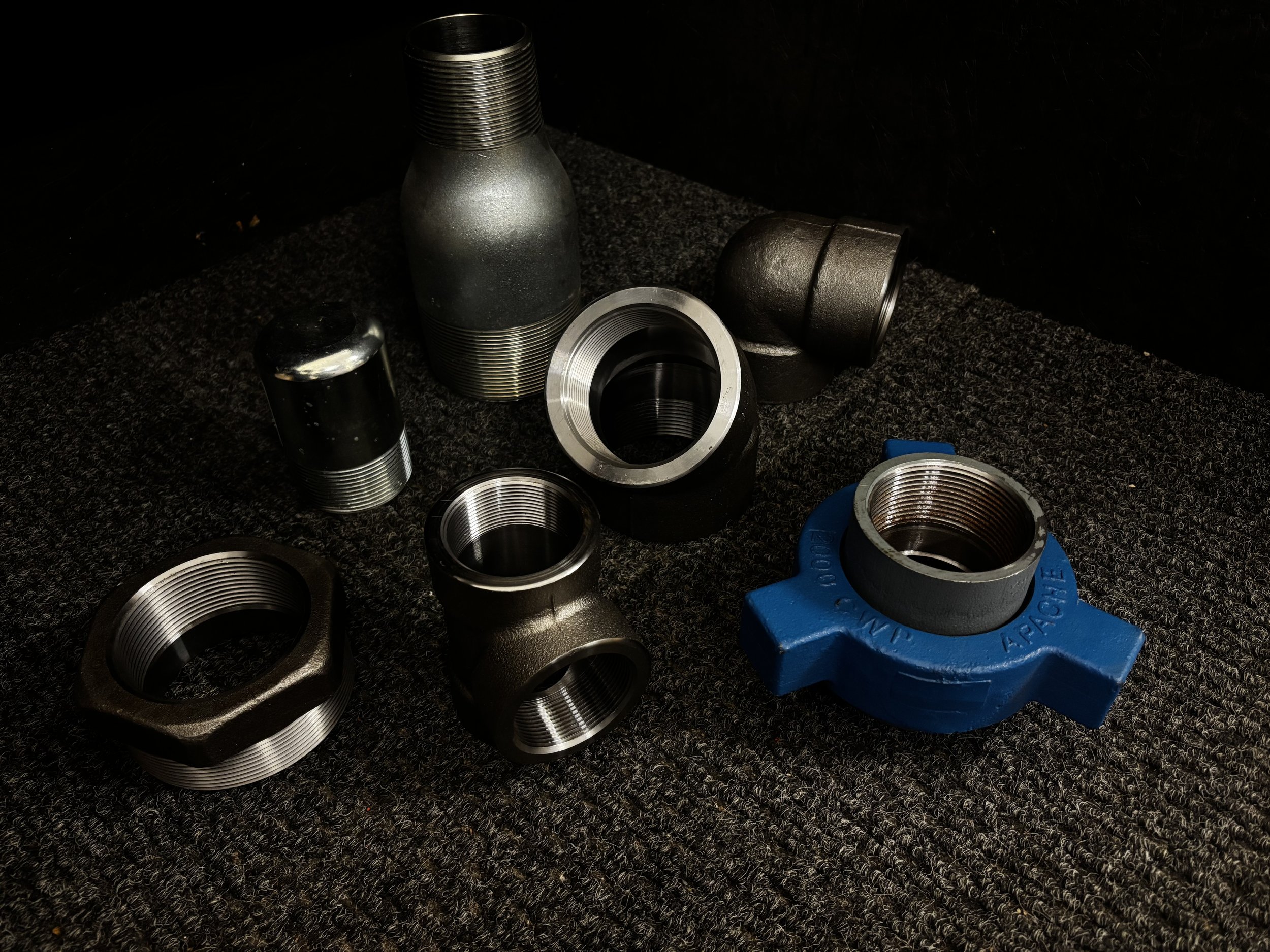 Various metal and plastic threaded pipe fittings and connectors on a dark textured surface.