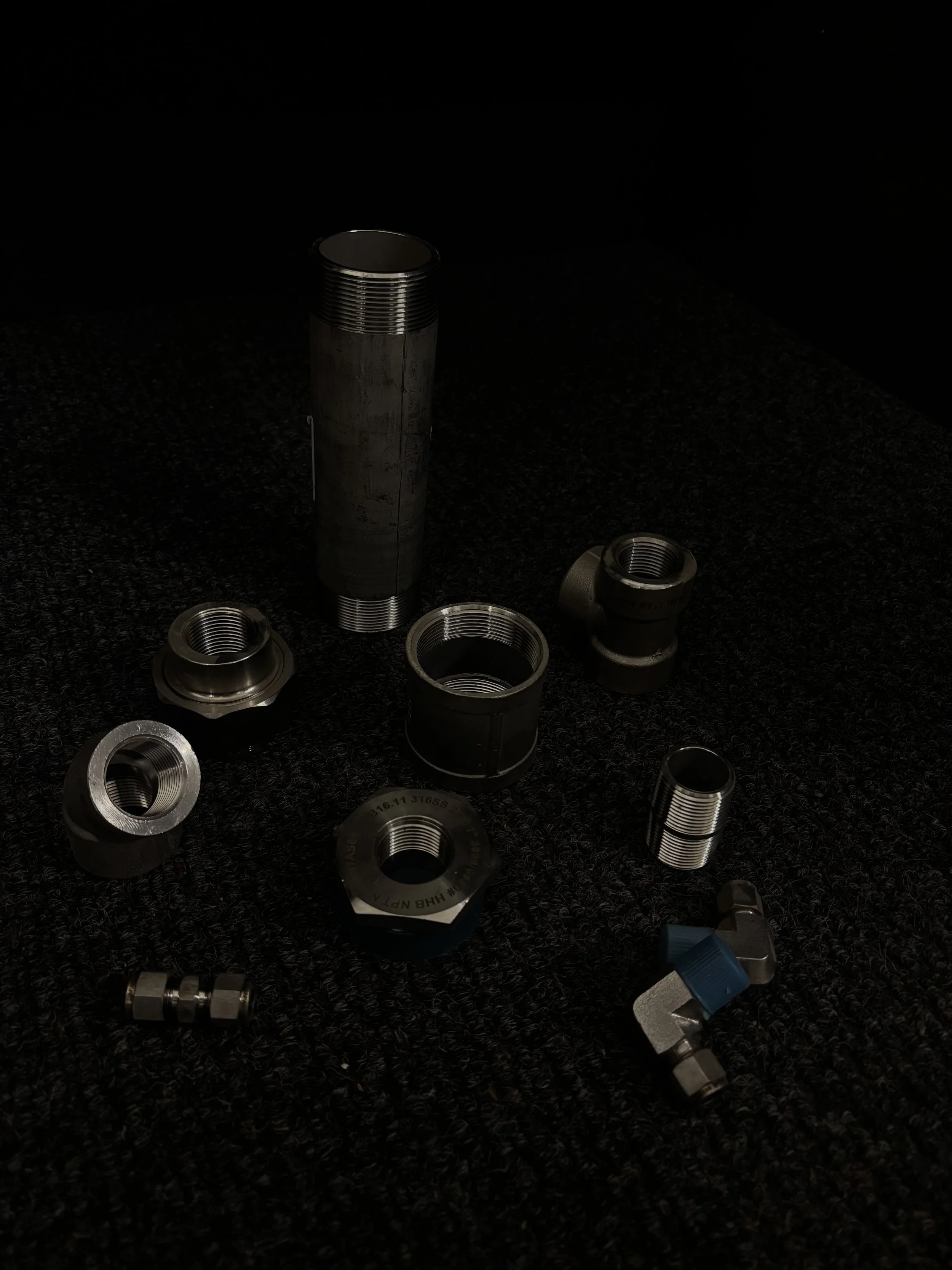 Collection of metal threaded fittings and connectors on a black textured surface.
