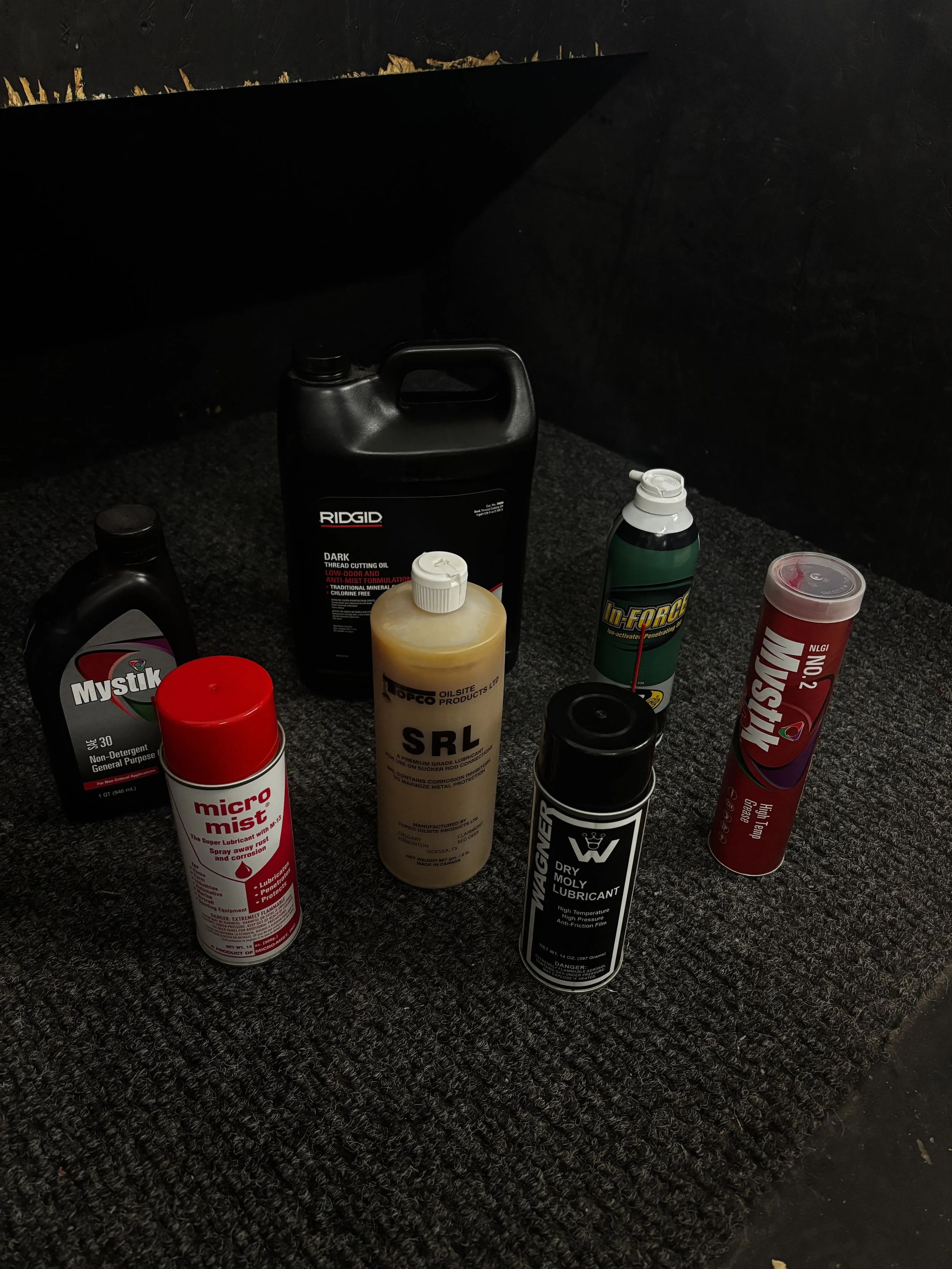 Various automotive lubricants and cleaning products arranged on a dark carpeted floor.