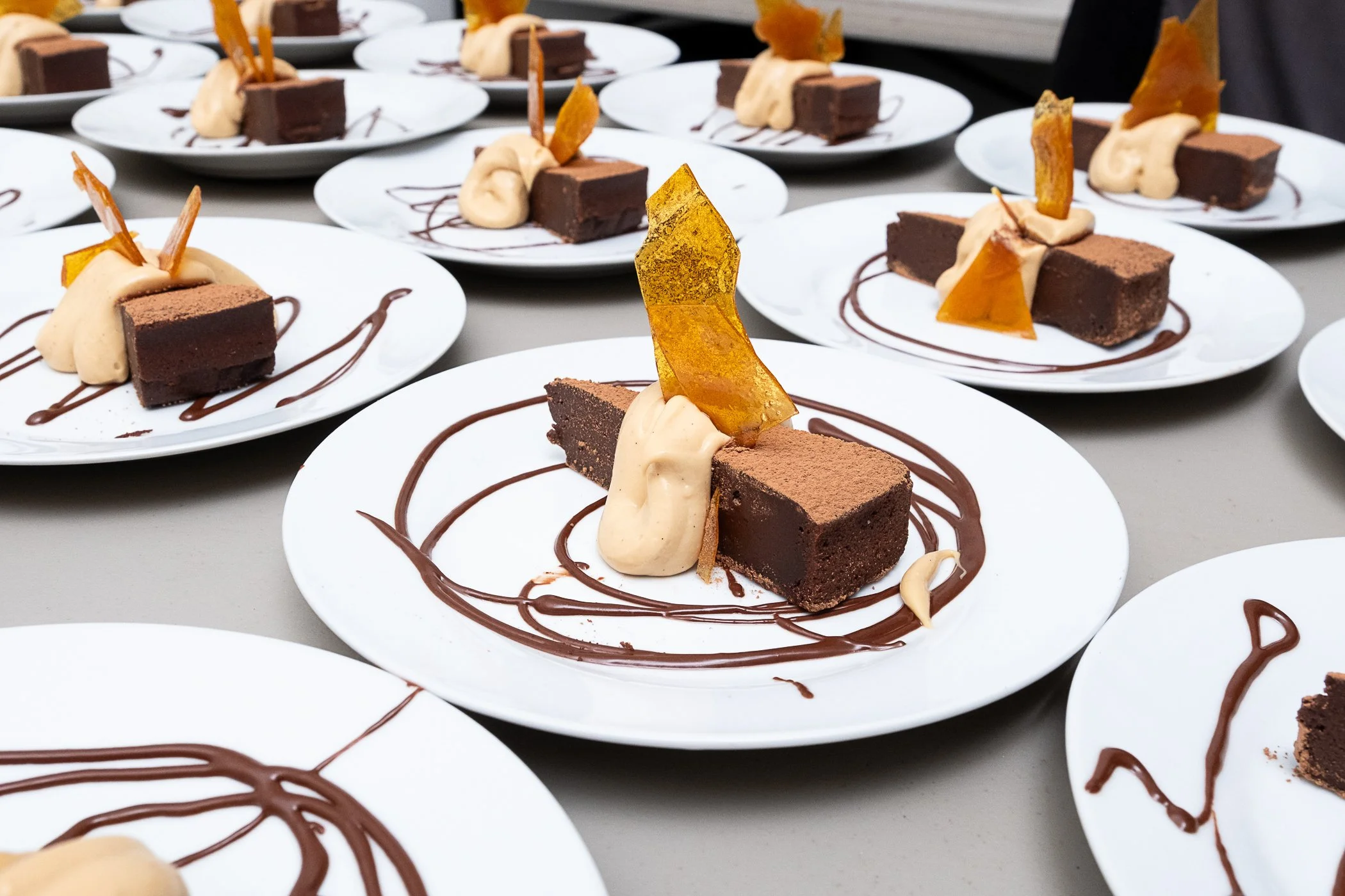 Plated chocolate cake slices with whipped cream and caramel shards for a catered dessert course