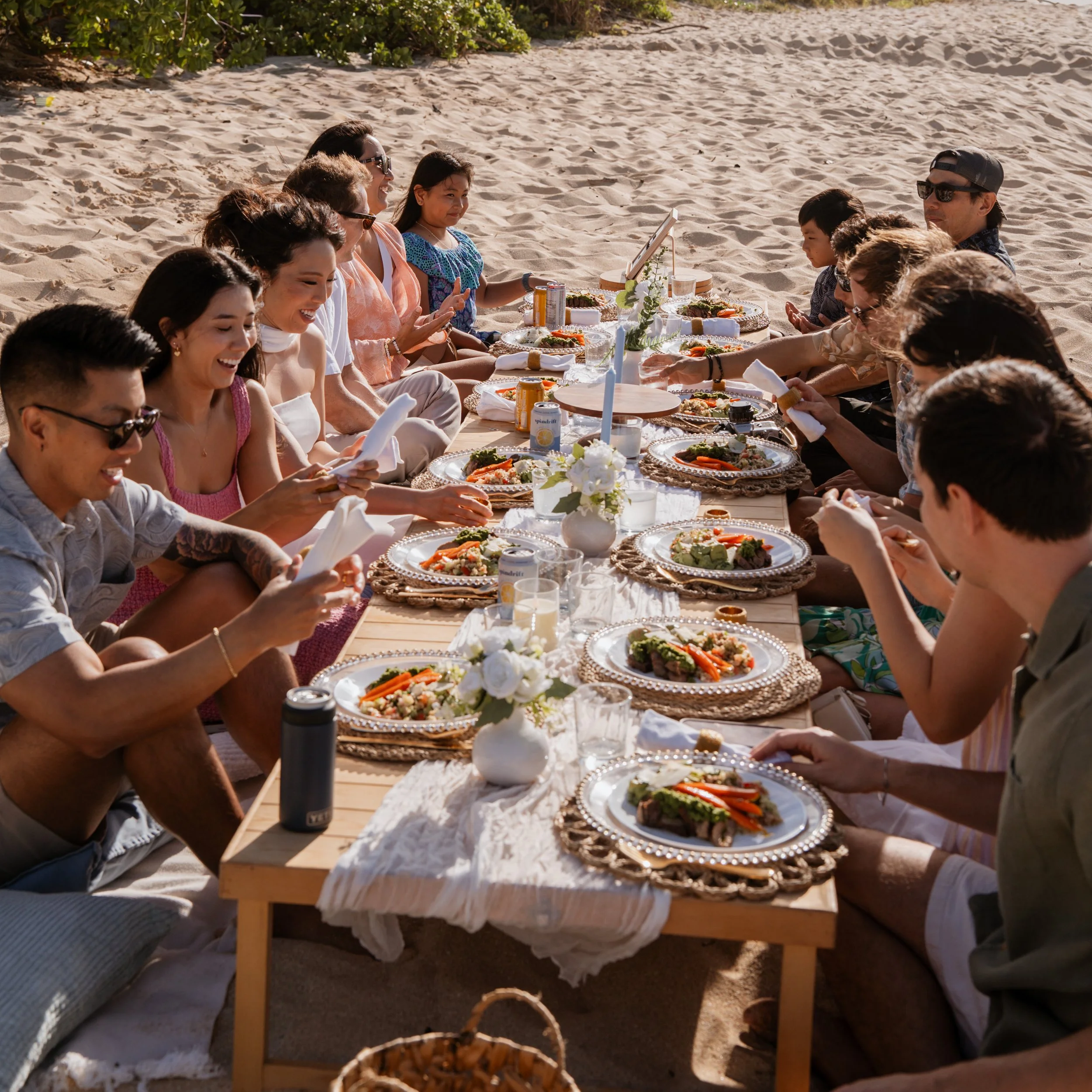 Guests enjoying a plated dinner at a long table set up on the beach