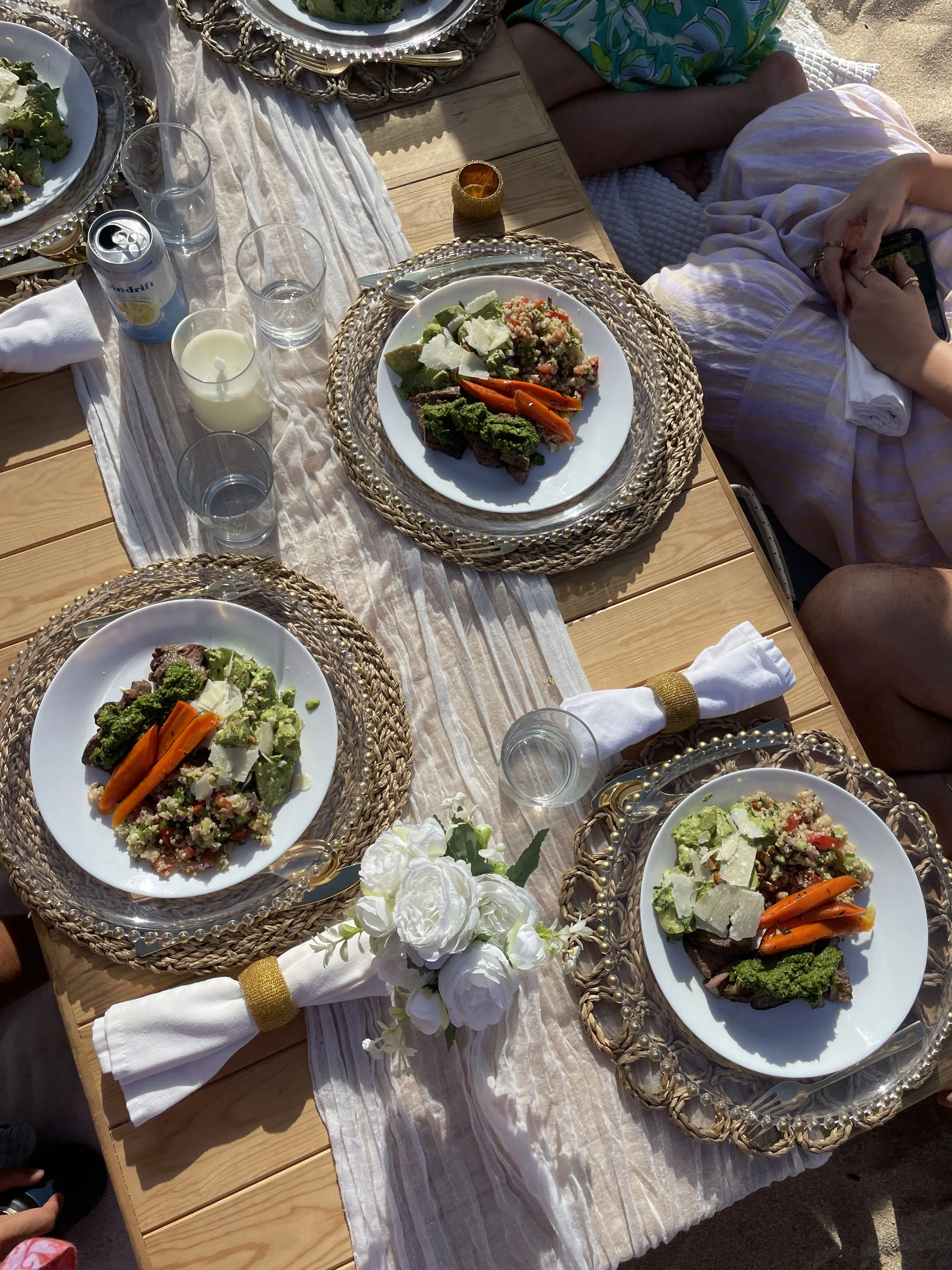 Plated dinners of sliced steak with chimichurri, roasted carrots and grain salad on woven chargers at a catered event